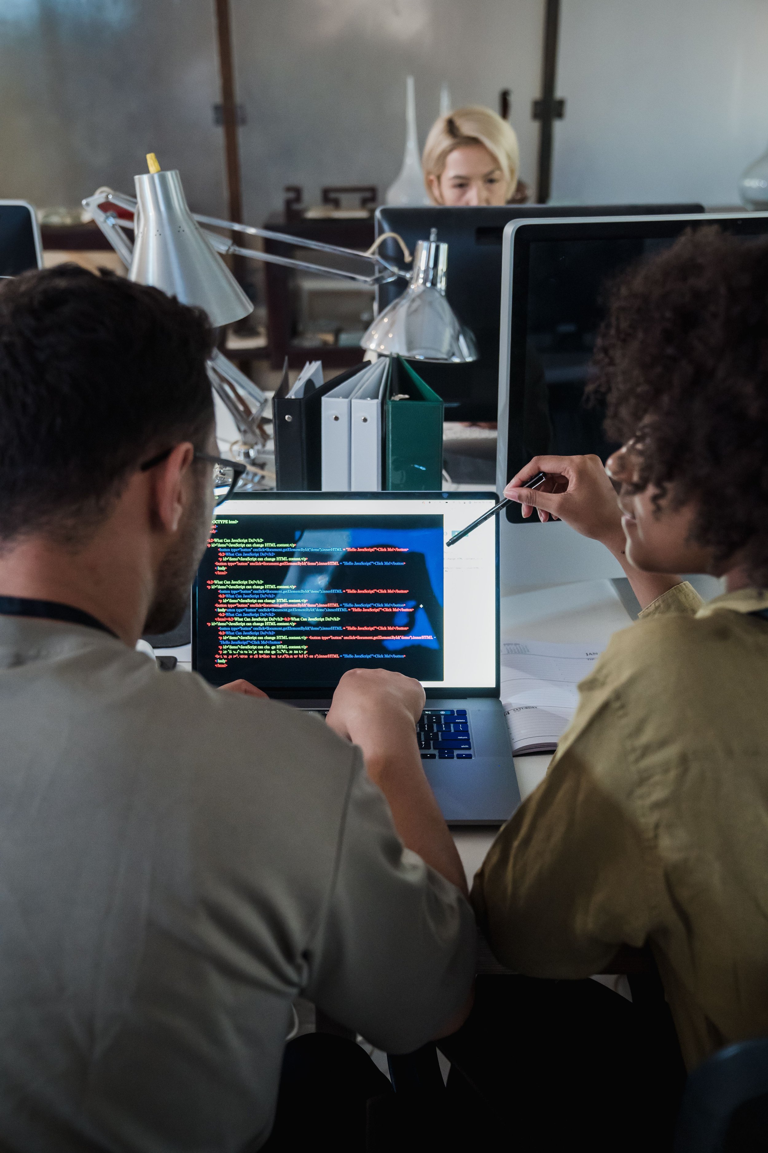 People working together at a table with a computer displaying code or a programming script.