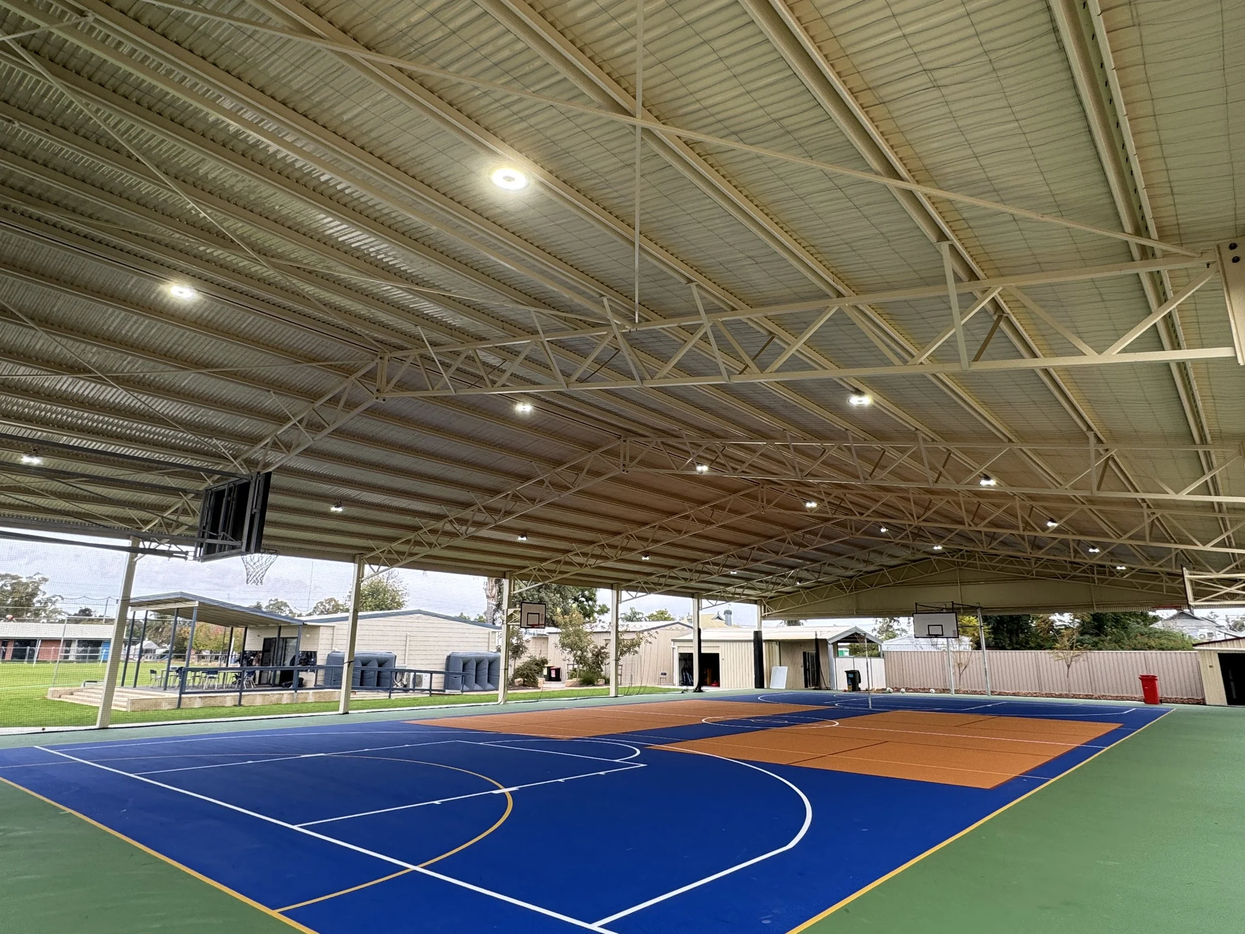 Empty basketball court inside a covered outdoor sports facility with basketball hoops and a high ceiling.