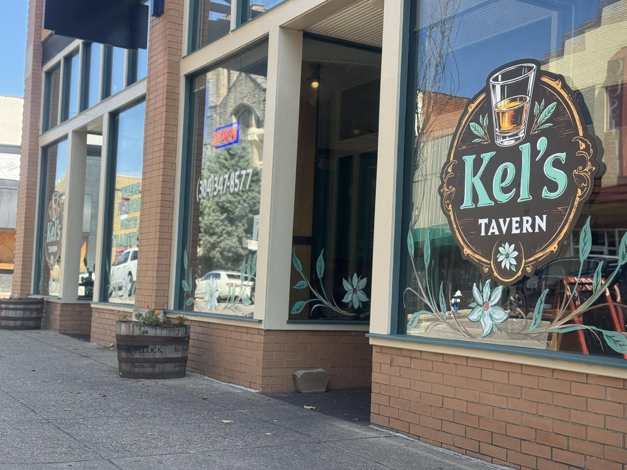 Exterior of a brick building housing Kel's Tavern, with large front windows decorated with floral designs and a sign featuring a glass of beer.