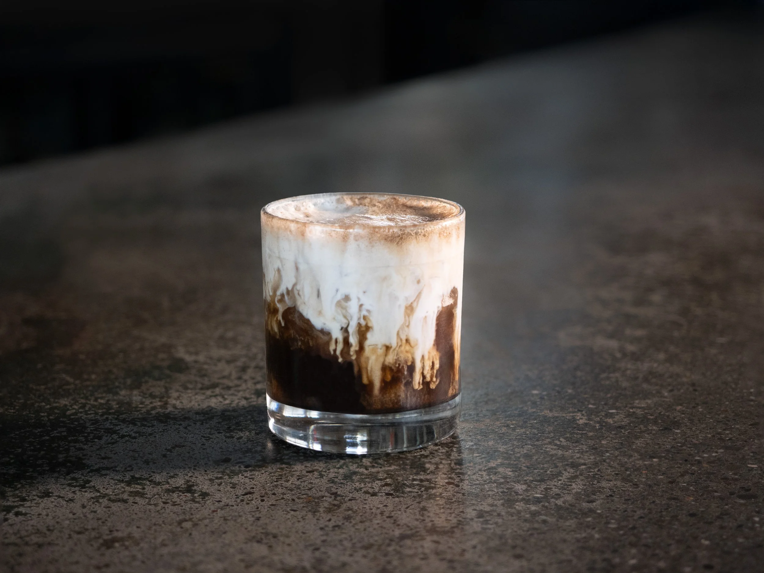 A glass of iced coffee with swirls of milk and chocolate syrup, placed on a dark countertop.