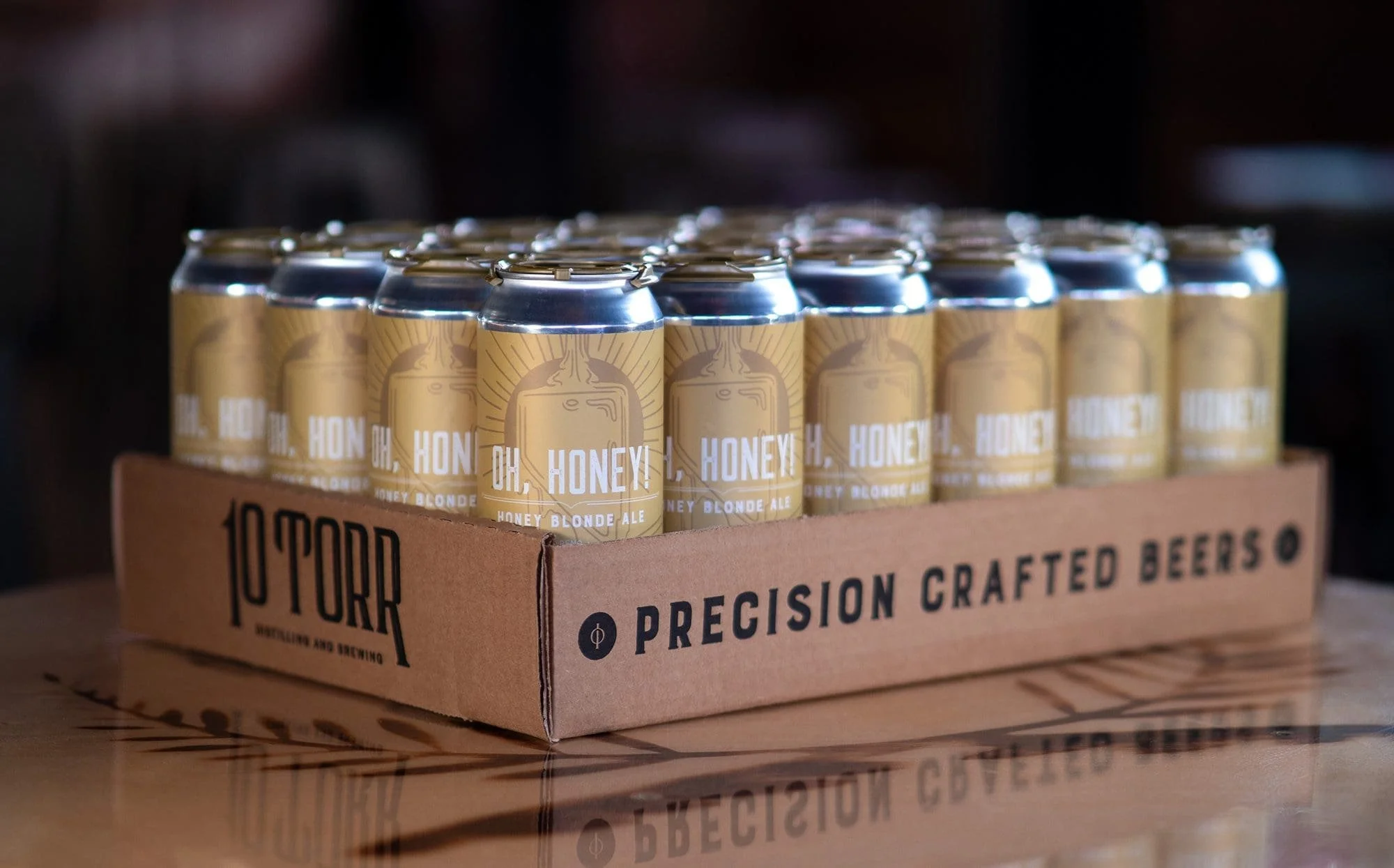 Multiple cans of honey blonde ale in a cardboard tray on a wooden surface.
