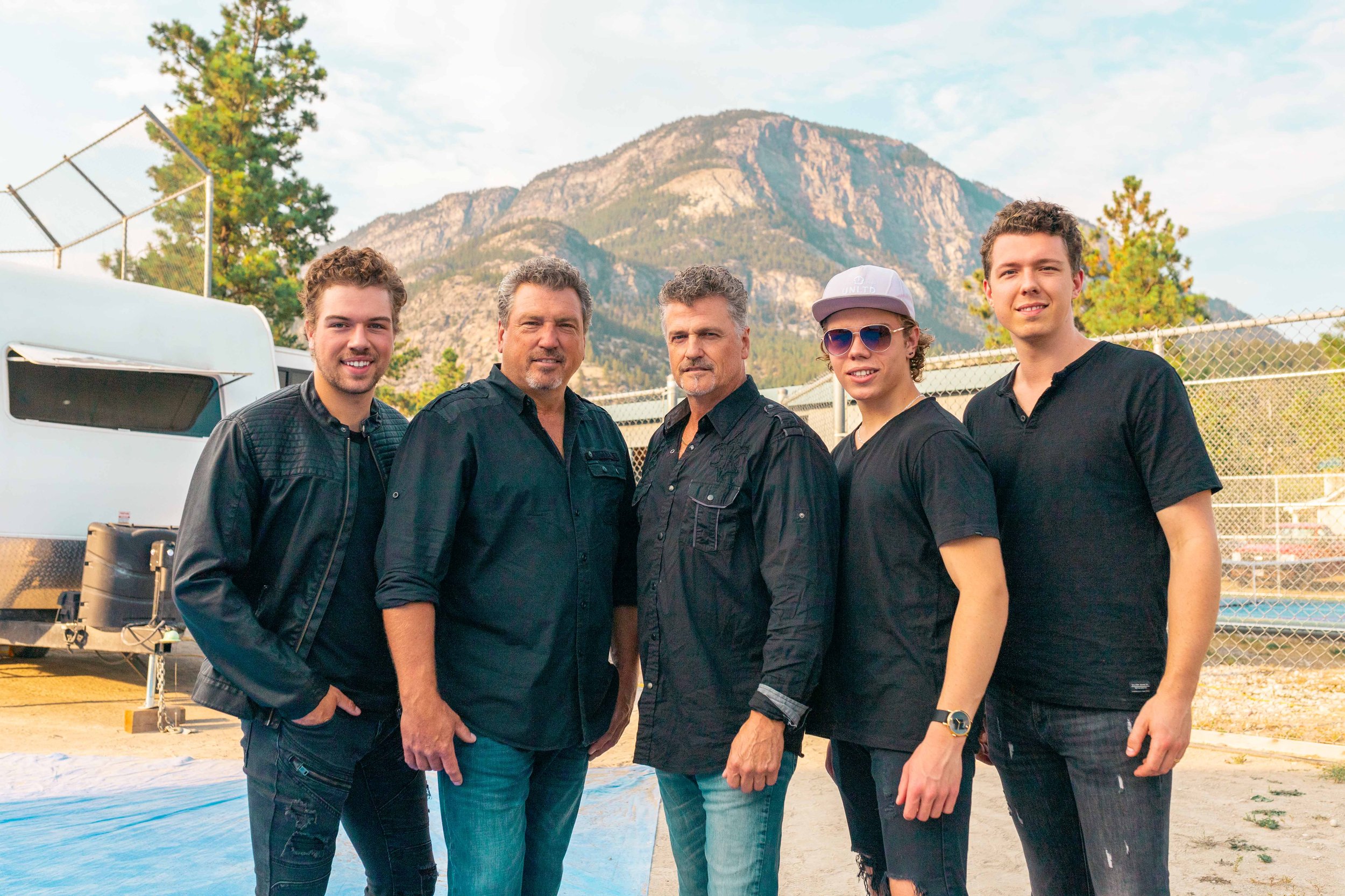 Johner Brothers. Five men standing outdoors with mountains in the background. They are dressed casually and looking at the camera.