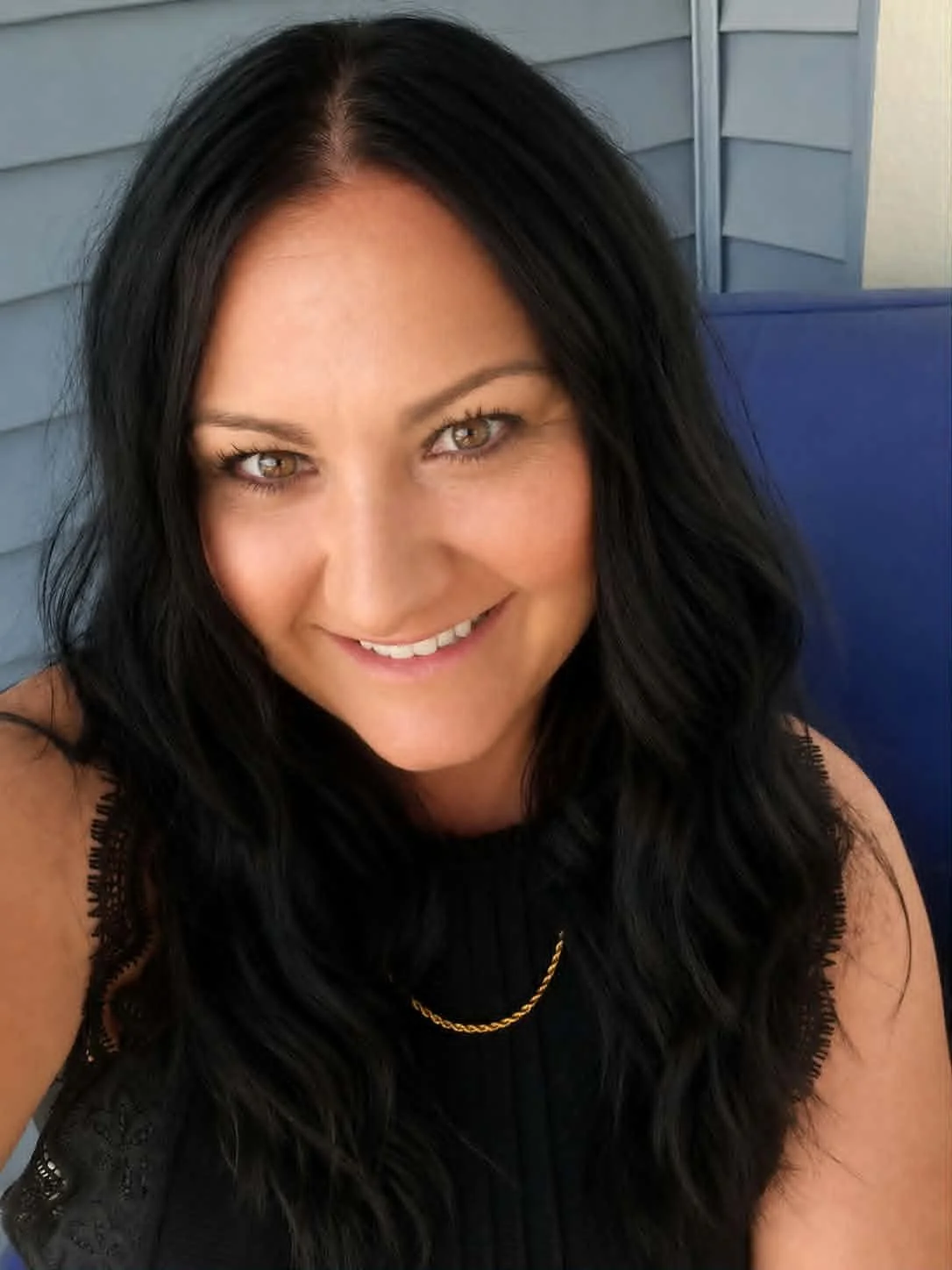 Close-up of a woman with black hair, brown eyes, and a black sleeveless top, smiling.