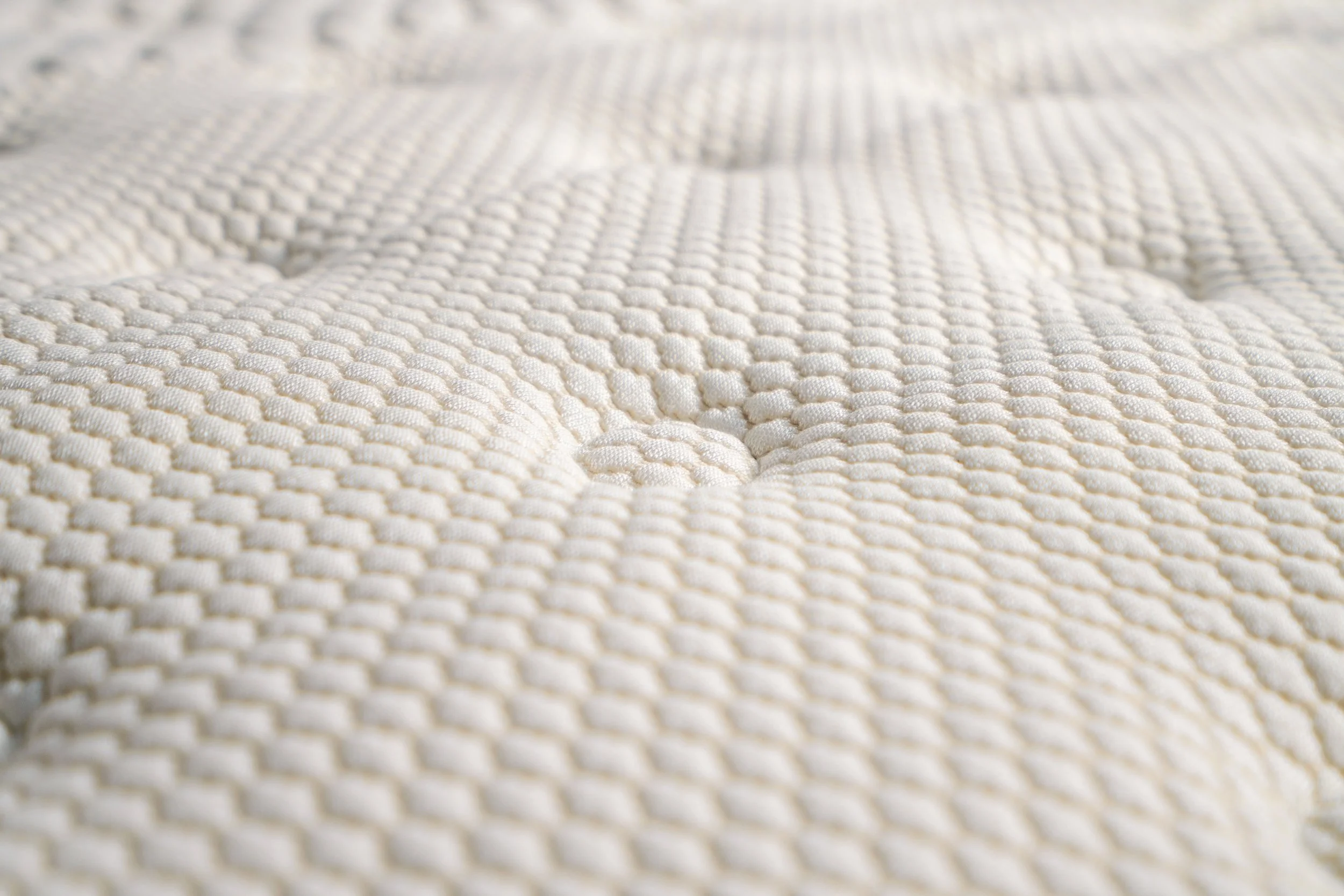 Close-up of cream knit mattress fabric with a raised quilted texture.