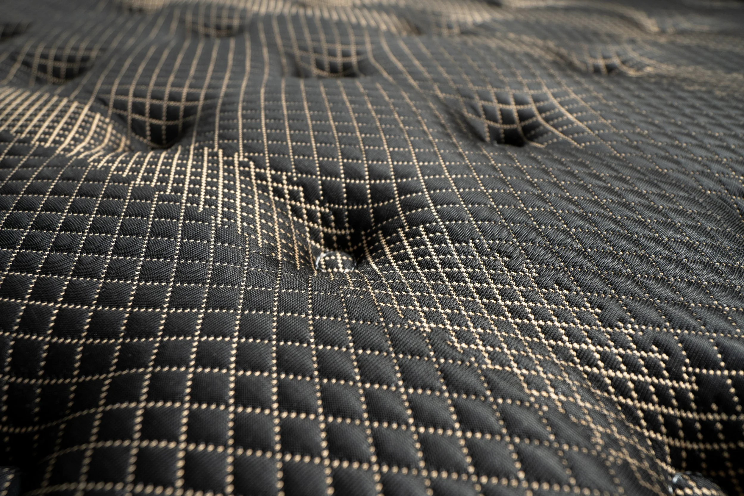 Close-up of the Midnight Diamond mattress’s black fabric, featuring plush tufting and an intricate gold geometric pattern.