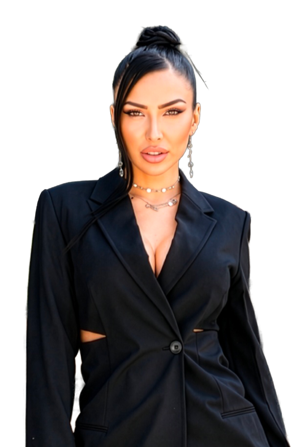 A woman with long dark hair styled in a high ponytail, wearing a black tailored blazer with cutouts, gold jewelry, including earrings, layered necklaces, and makeup with defined eyebrows and nude lipstick.
