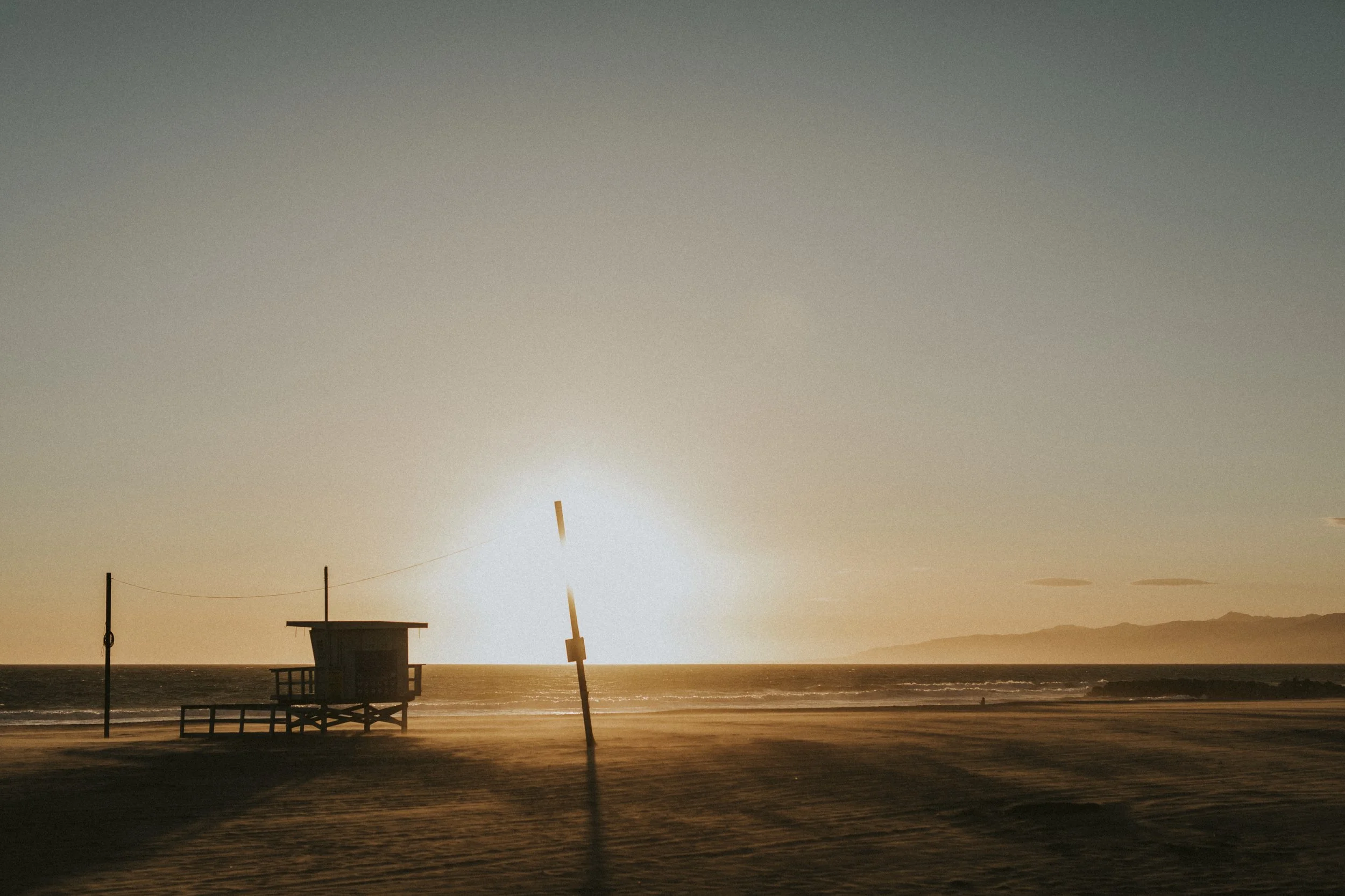 Beach scene with lifeguard tower and poles during sunset or sunrise.