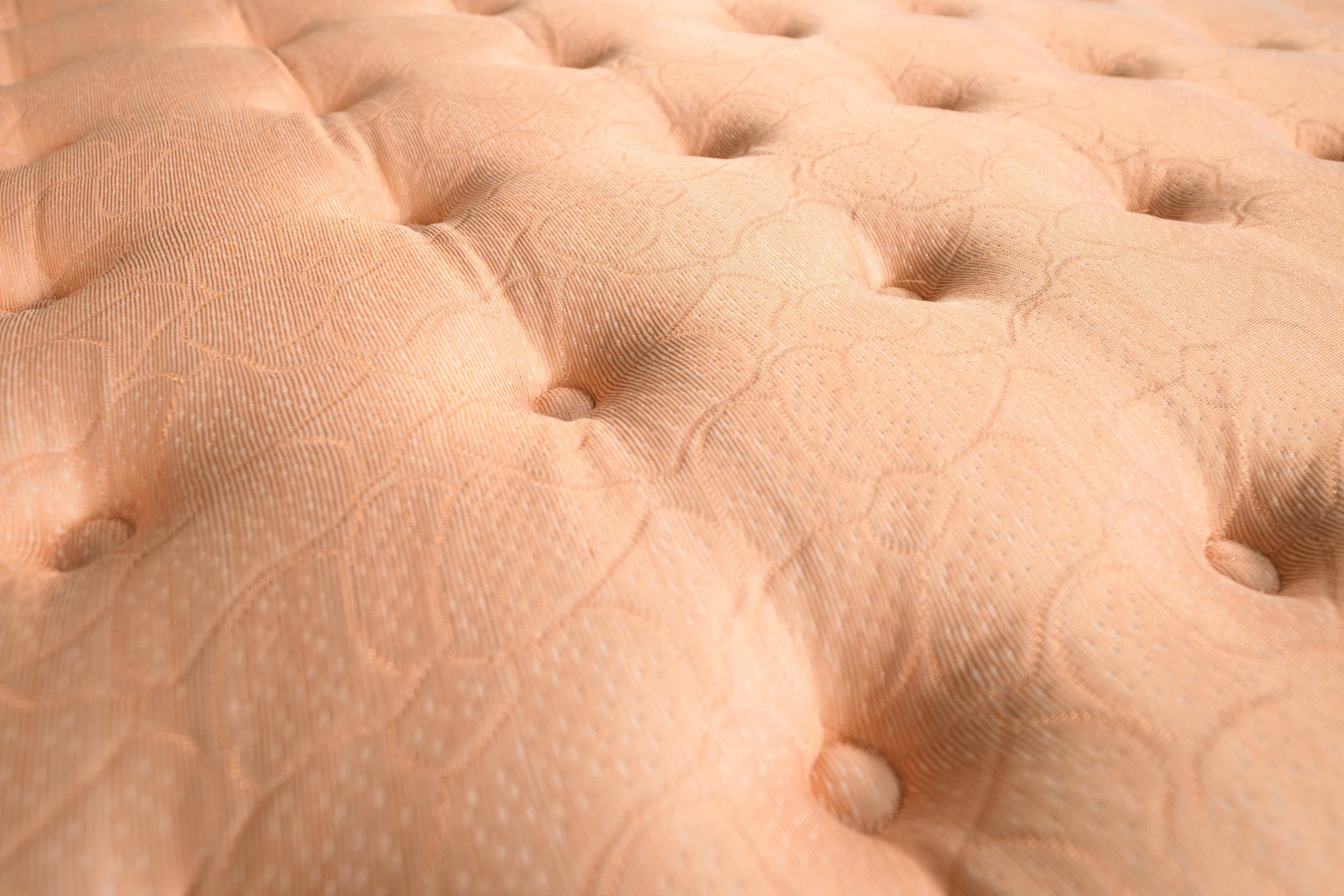 Close-up of rose gold mattress fabric with plush tufting.