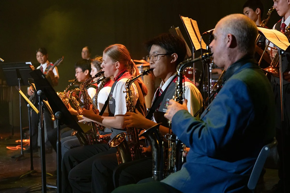 Group of students and Andy Firth playing saxophones in a big band, performing on stage.