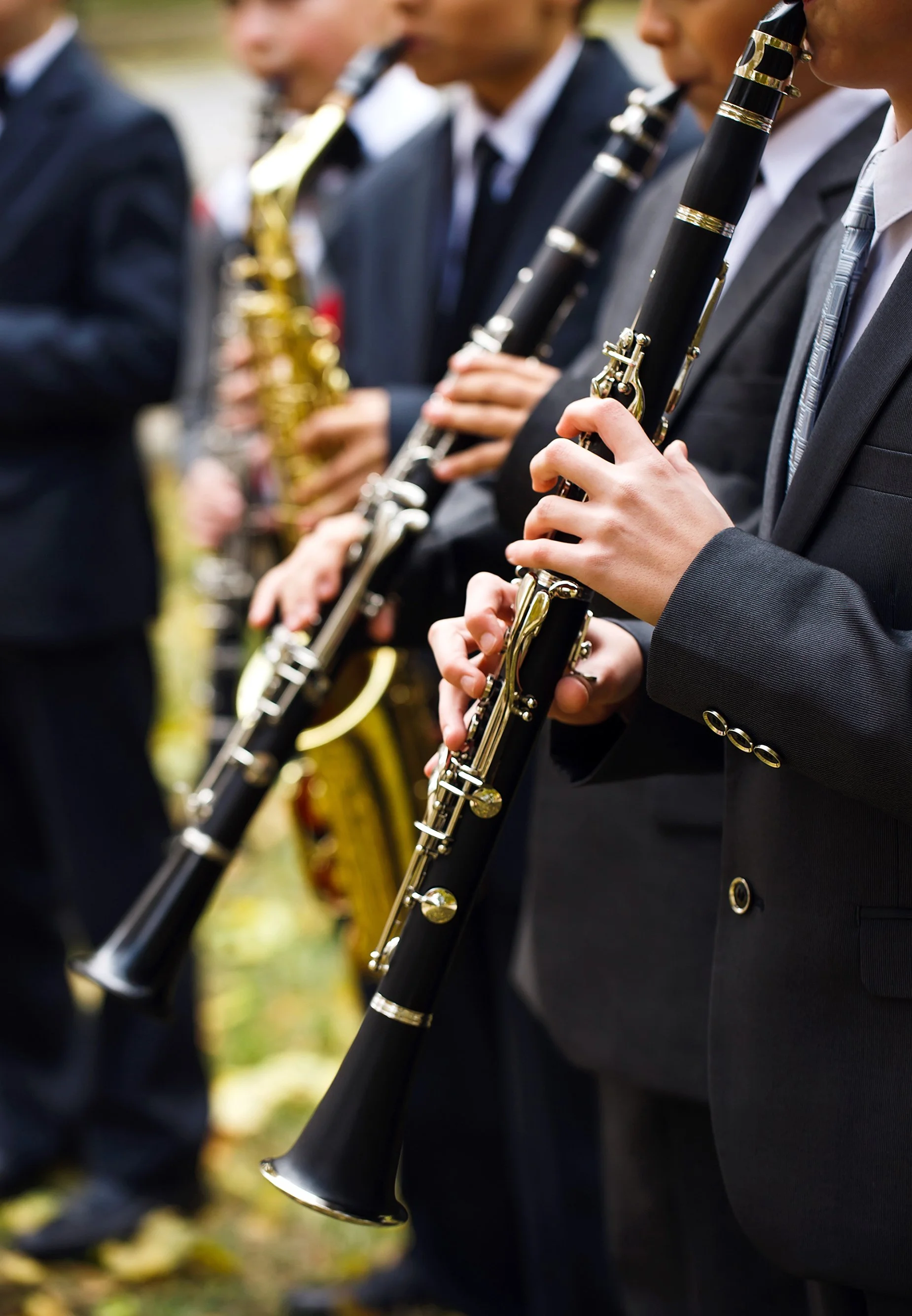 Group of musicians dressed in suits playing clarinets at an outdoor event.