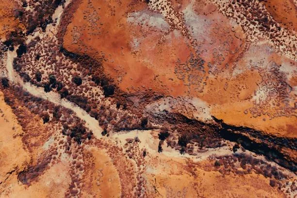 Aerial view of a desert landscape with reddish-brown rock formations, sparse vegetation, and dirt roads.