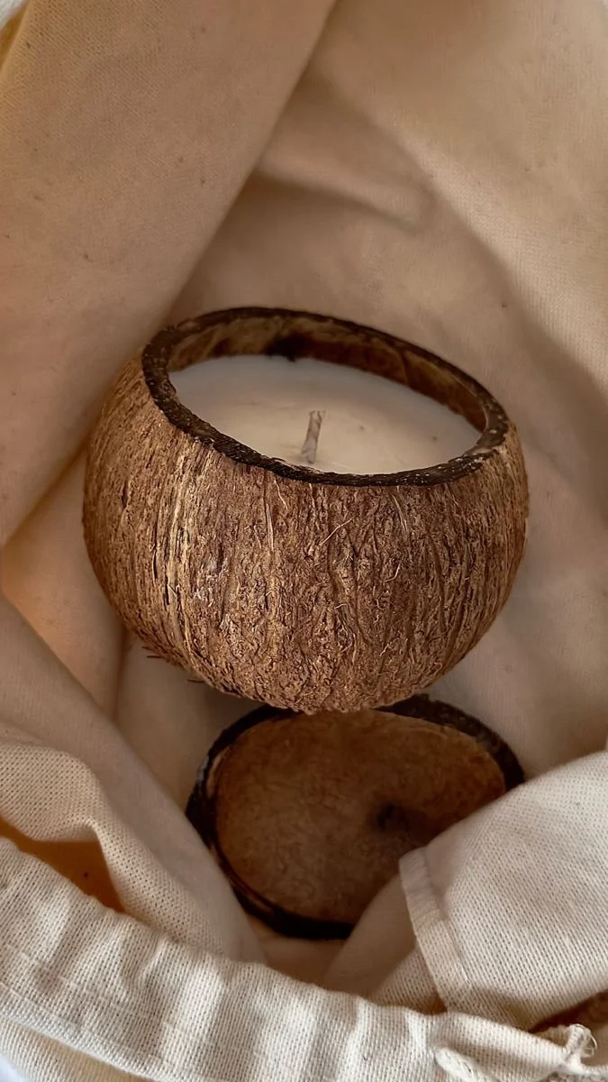 A round candle holder made from a coconut shell with a white candle inside, placed on light-colored fabric.
