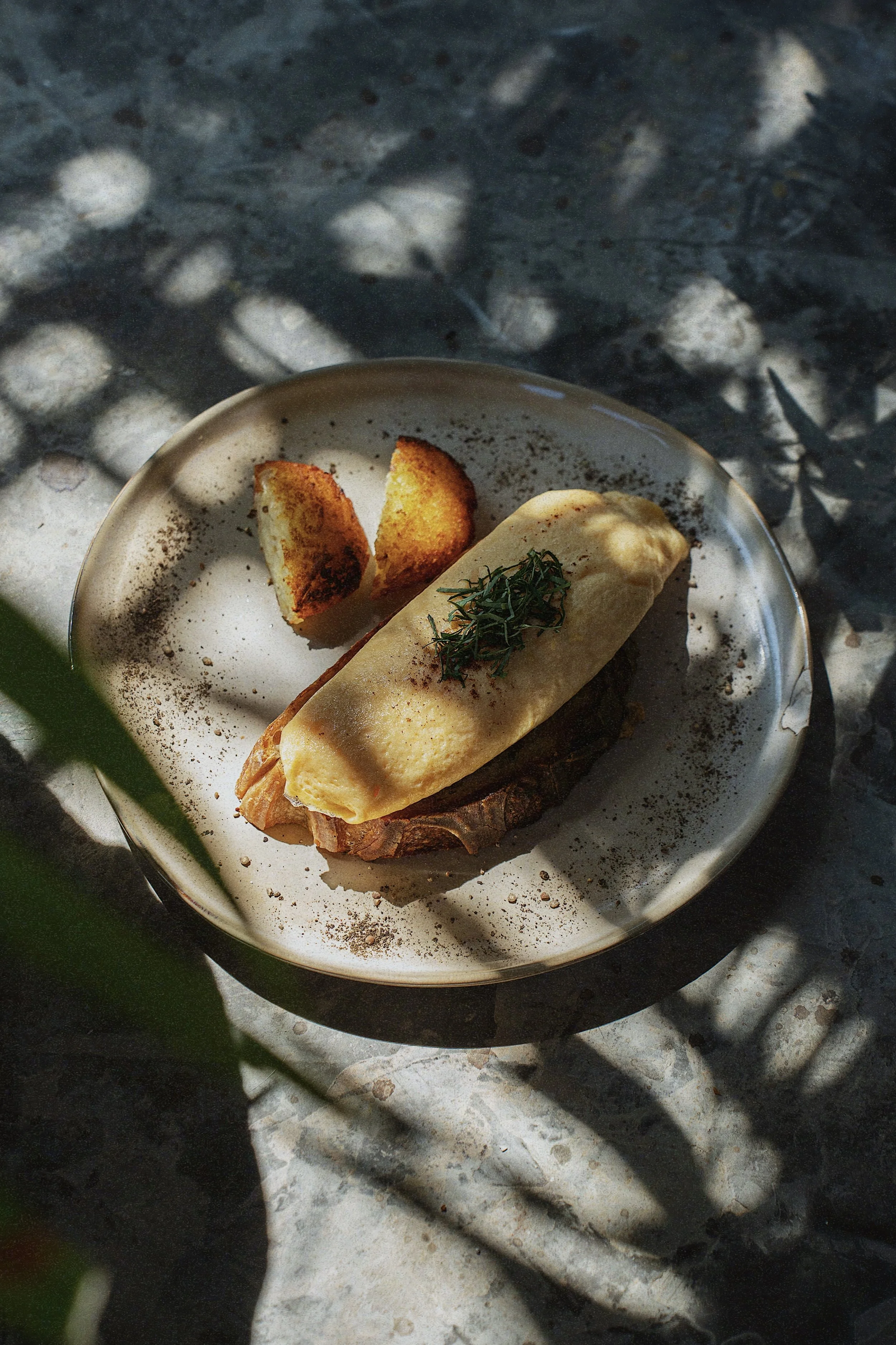 A plate with a piece omelette topped with herbs and two roasted potato wedges, garnished with black pepper and paprika.