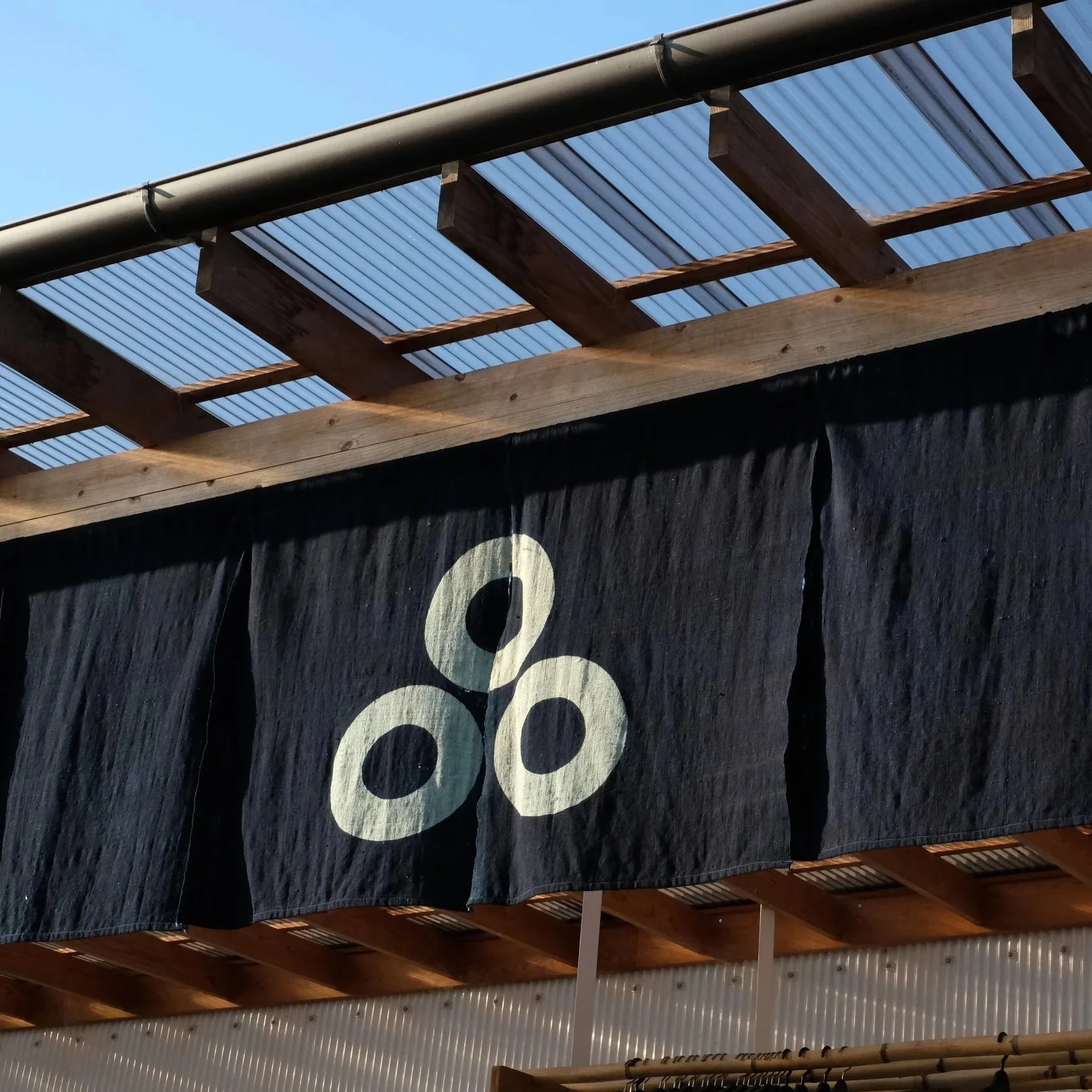 A indigo fabric banner with large white numbers attached to a wooden structure, with part of a metal beam and a roof of wooden slats visible overhead.