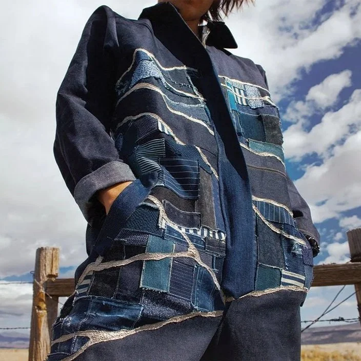 Person wearing a patchwork denim jacket with hands in pockets outdoors on a cloudy day.