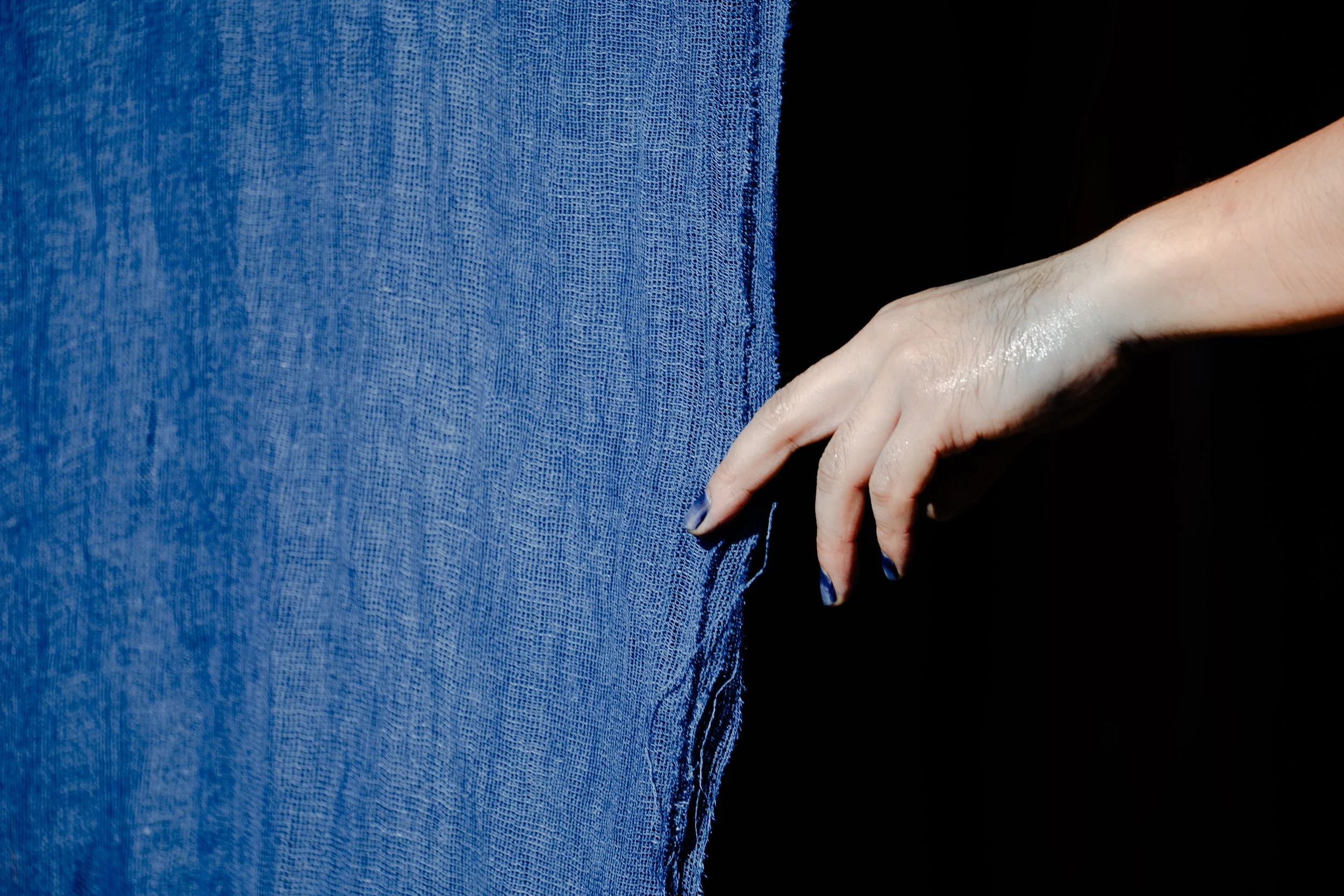 Close-up of a person's hand resting on their hip, wearing blue jeans against a black background.