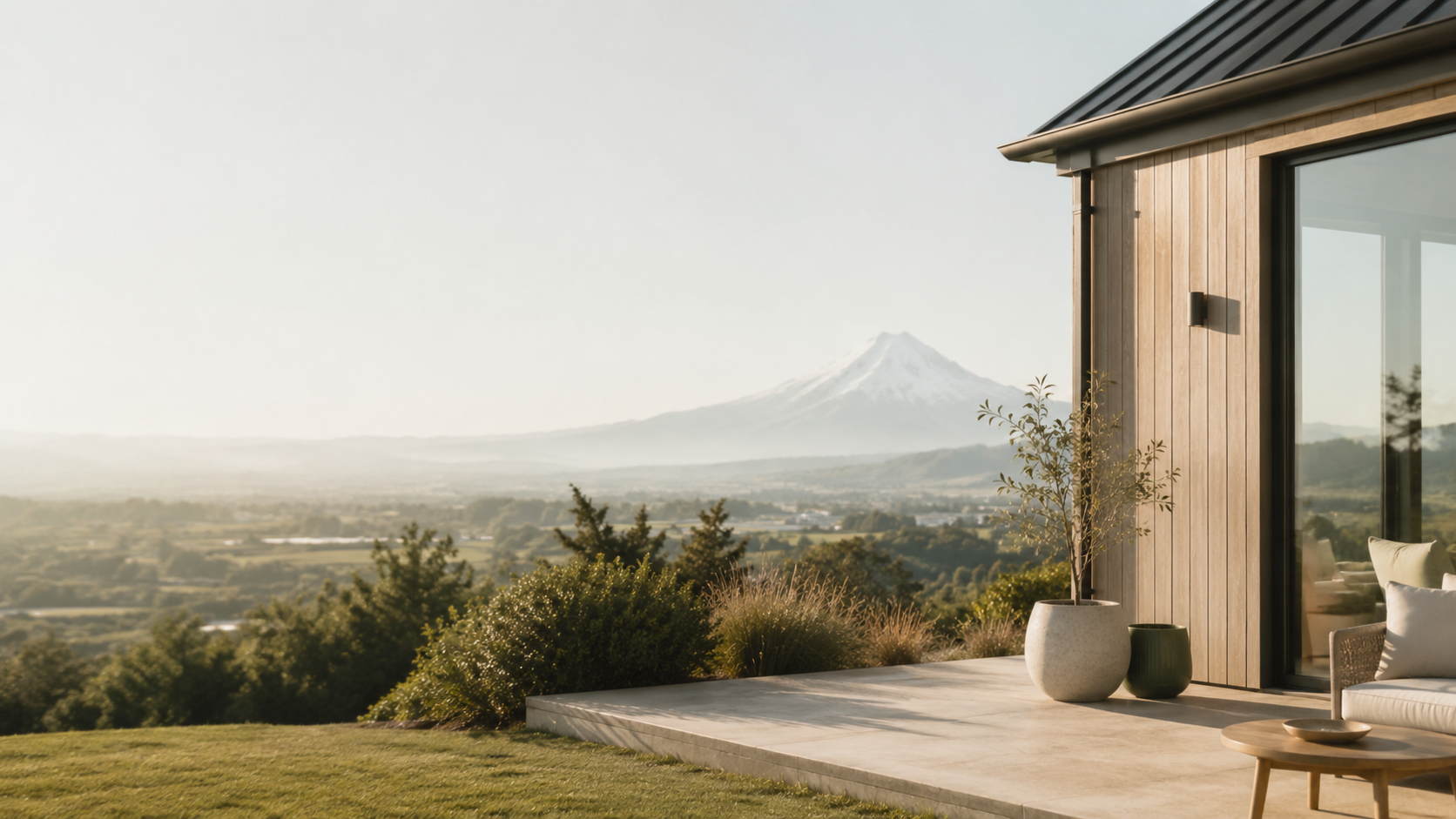 A modern house patio with potted plants and a view of a mountainous landscape, including a snow-capped peak.