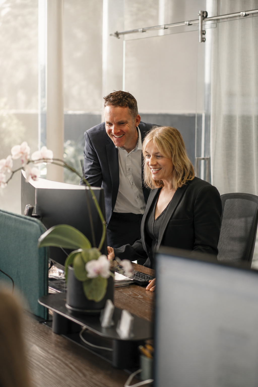 A man and woman look at a computer screen and smile in an office setting.