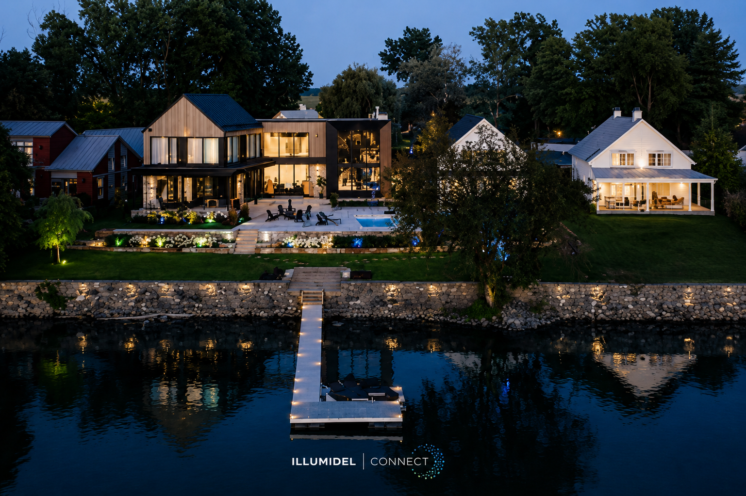 A modern home with large glass windows, a swimming pool, a deck with outdoor furniture, and a dock extending into a body of water, illuminated at night with exterior lights and interior lights visible through the windows.