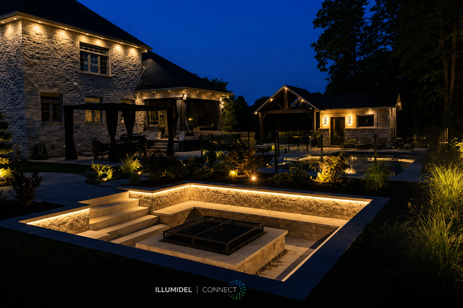 Nighttime view of a luxurious backyard with a stone house, illuminated outdoor lighting, a patio with seating, and landscaped garden with subtle lighting, featuring a fire pit surrounded by stone steps.