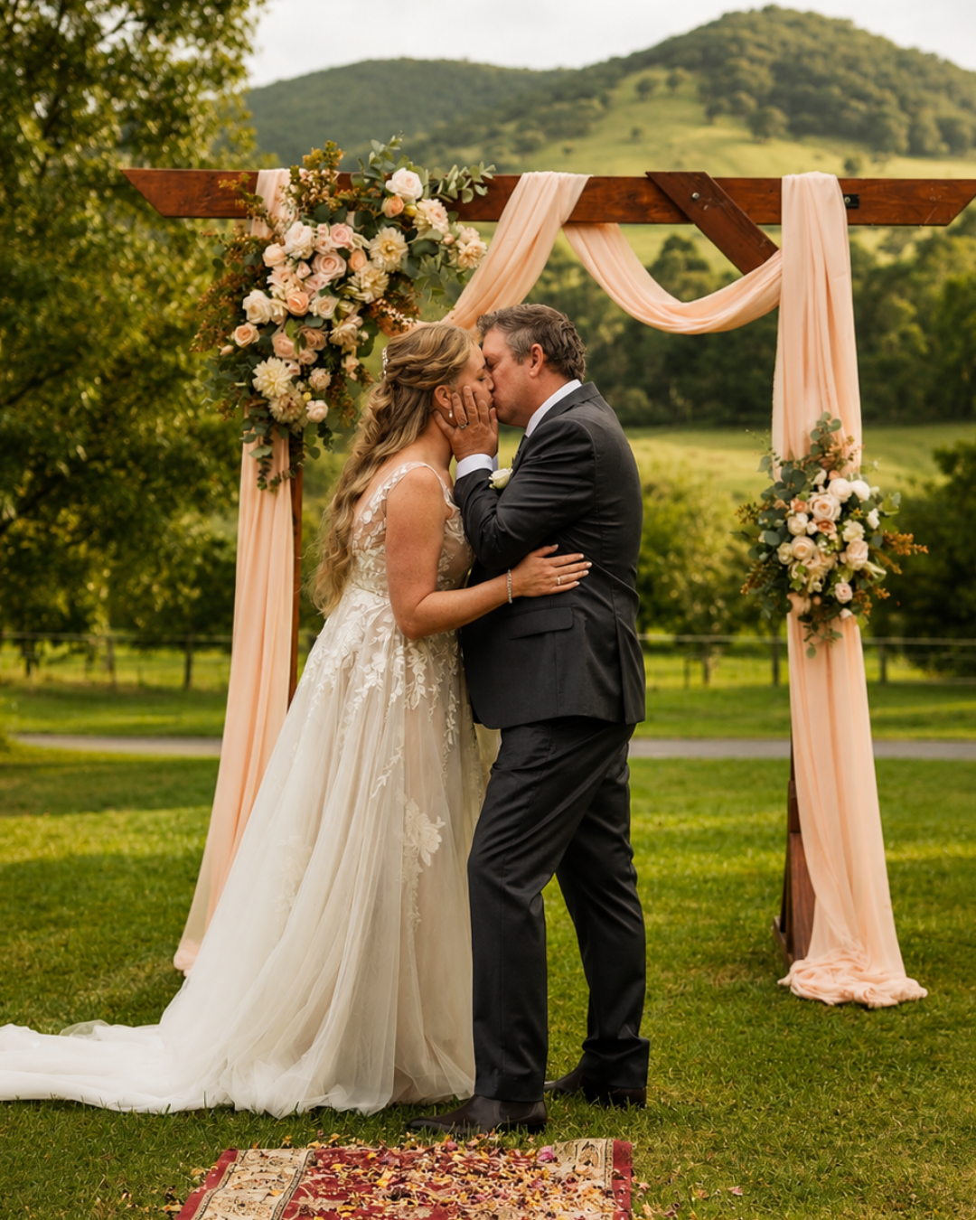 Outdoor wedding ceremony beneath a flower-covered wedding arch, surrounded by natural greenery.