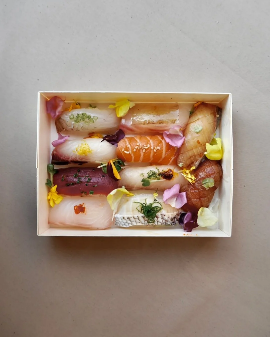 Assorted sushi pieces with edible flowers and garnishes in a white box