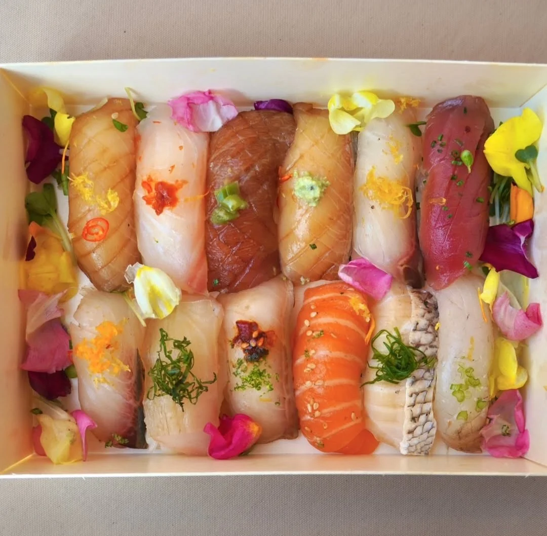 Assorted pieces of sushi with different types of fish and toppings, garnished with colorful flower petals.