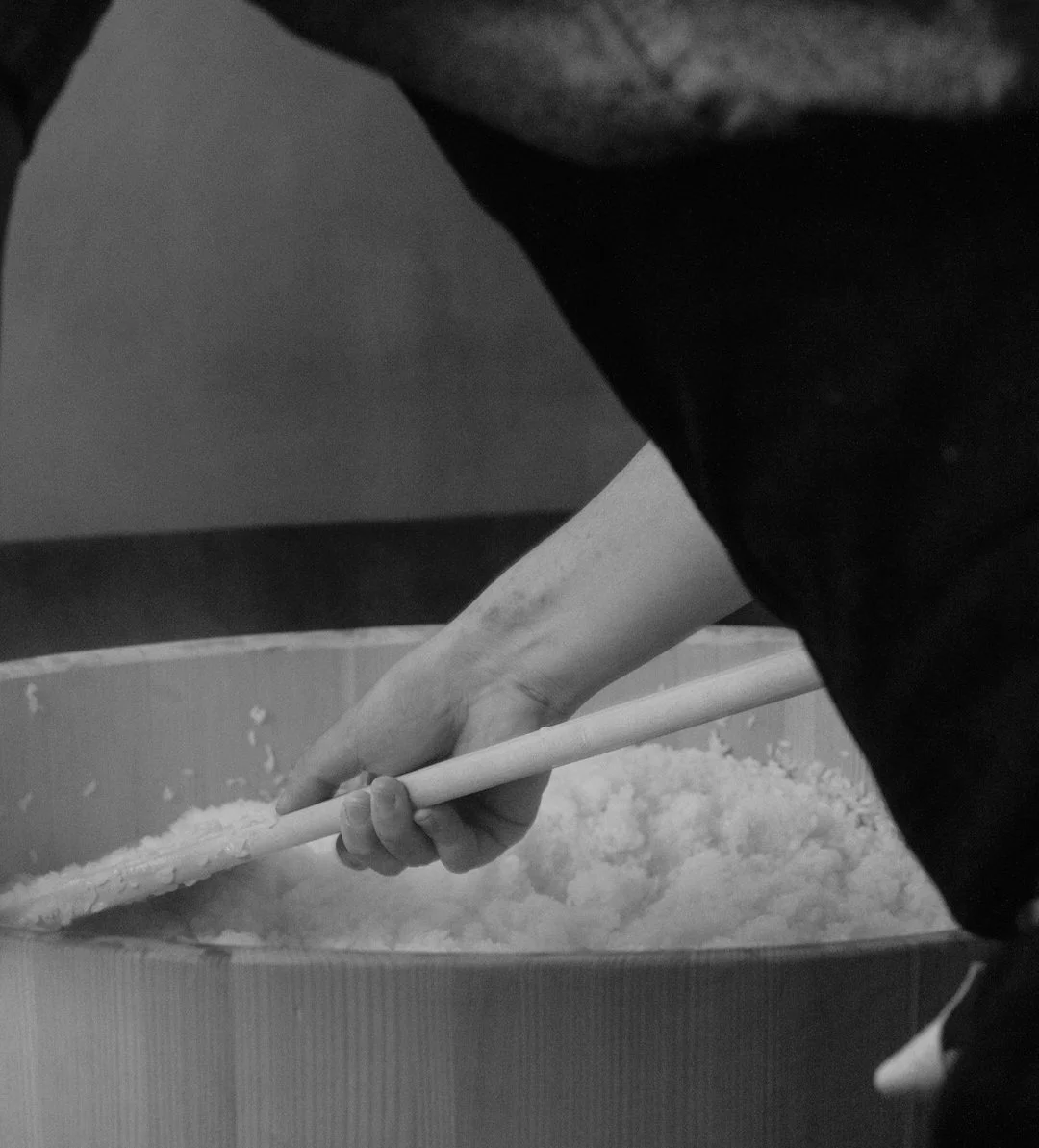 Close-up of a person stirring a large bowl of white powder with a long-handled spoon.