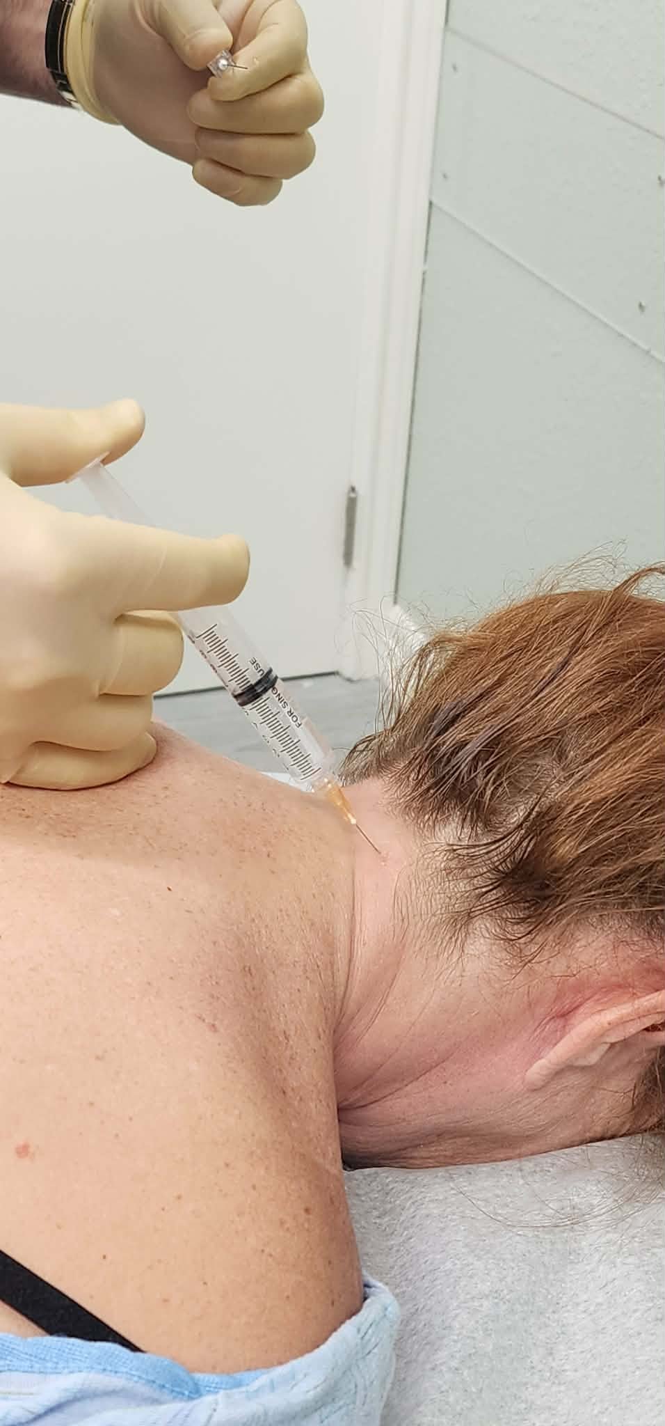 A person receiving an injection in the neck, with a healthcare worker preparing the syringe.