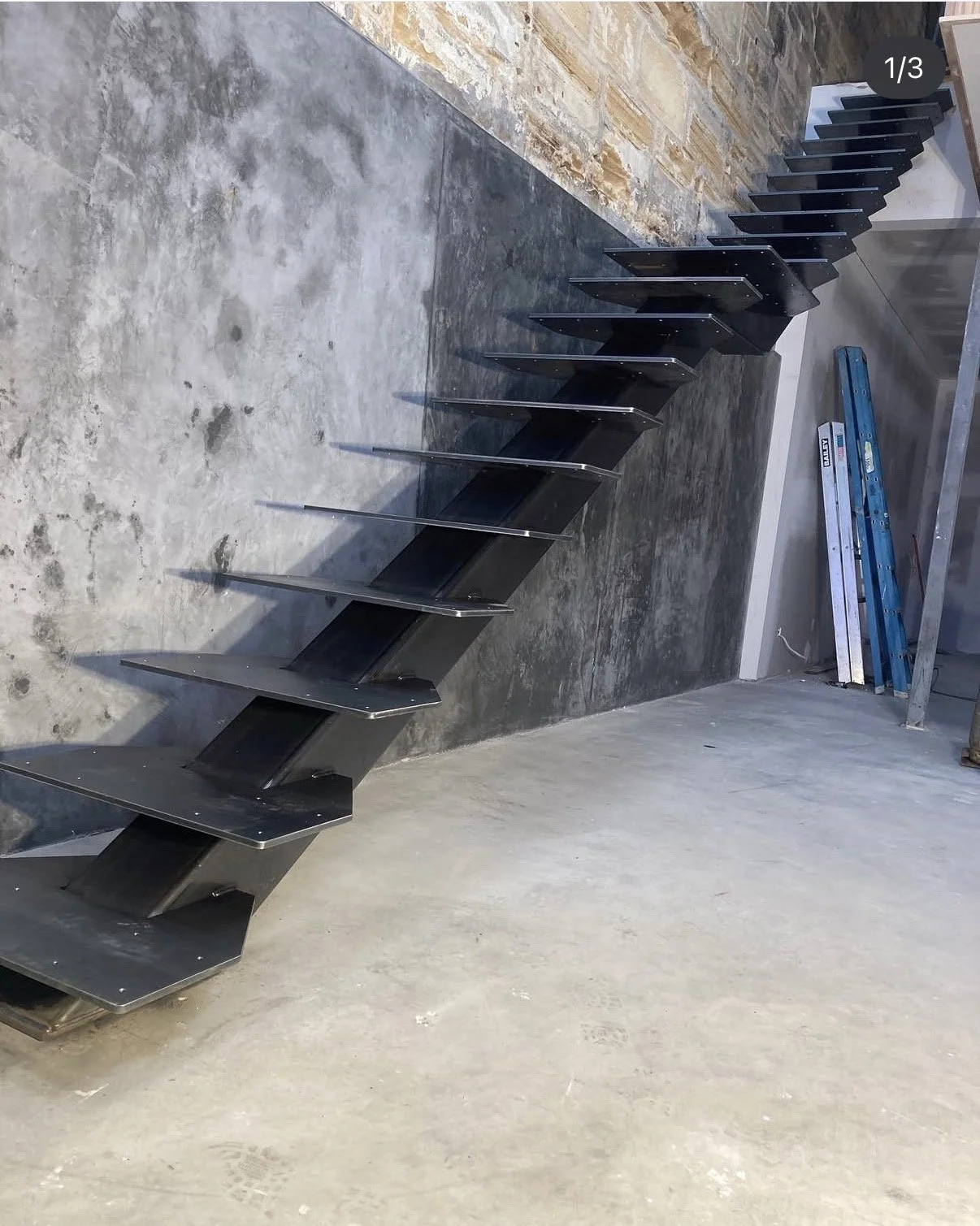 Metal staircase with zigzag design leaning against a wall in a room under construction or renovation.