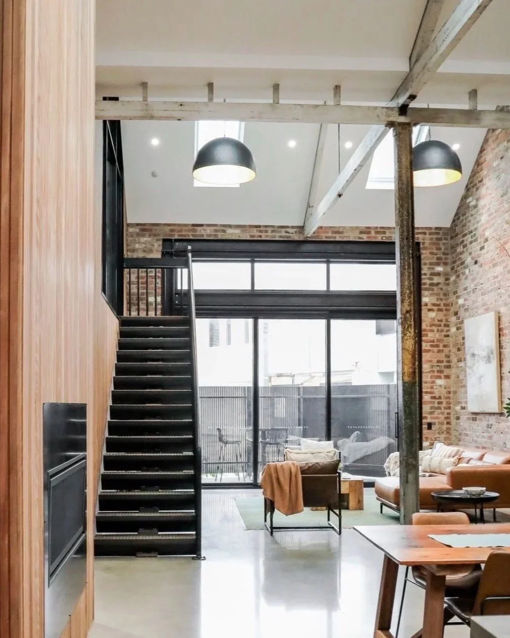 Open-concept living space with brick walls, skylights, black staircase, and modern furnishings
