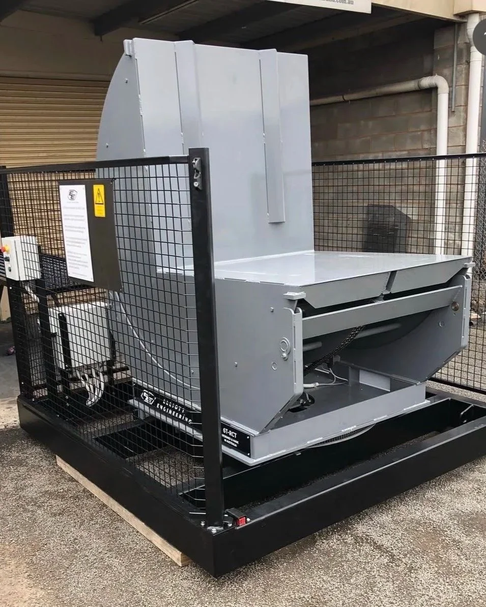 Large industrial machine with gray and black components, enclosed within a black metal safety cage, situated outdoors on a concrete ground.