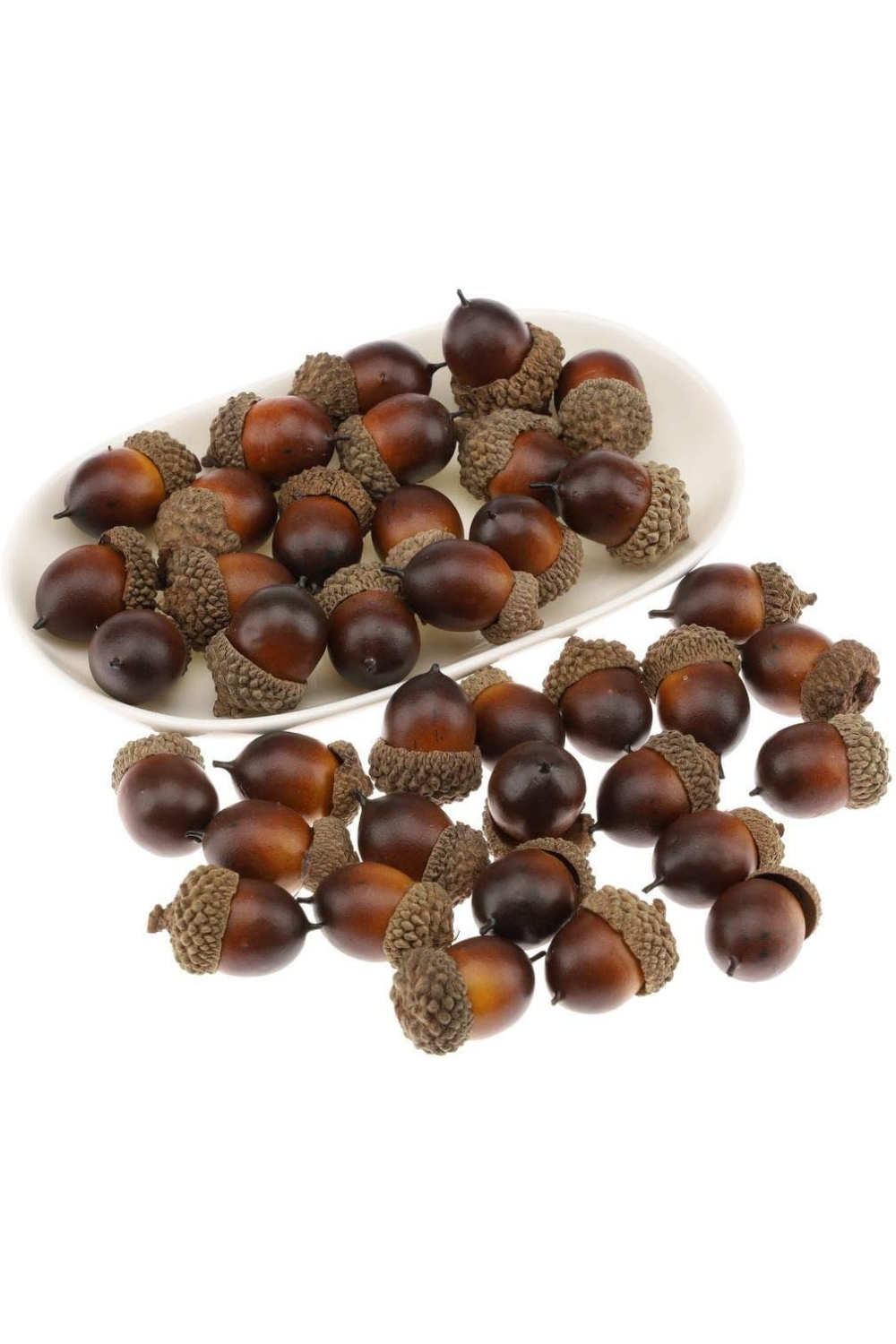A white oval dish filled with acorns, with some spilled onto a white surface.