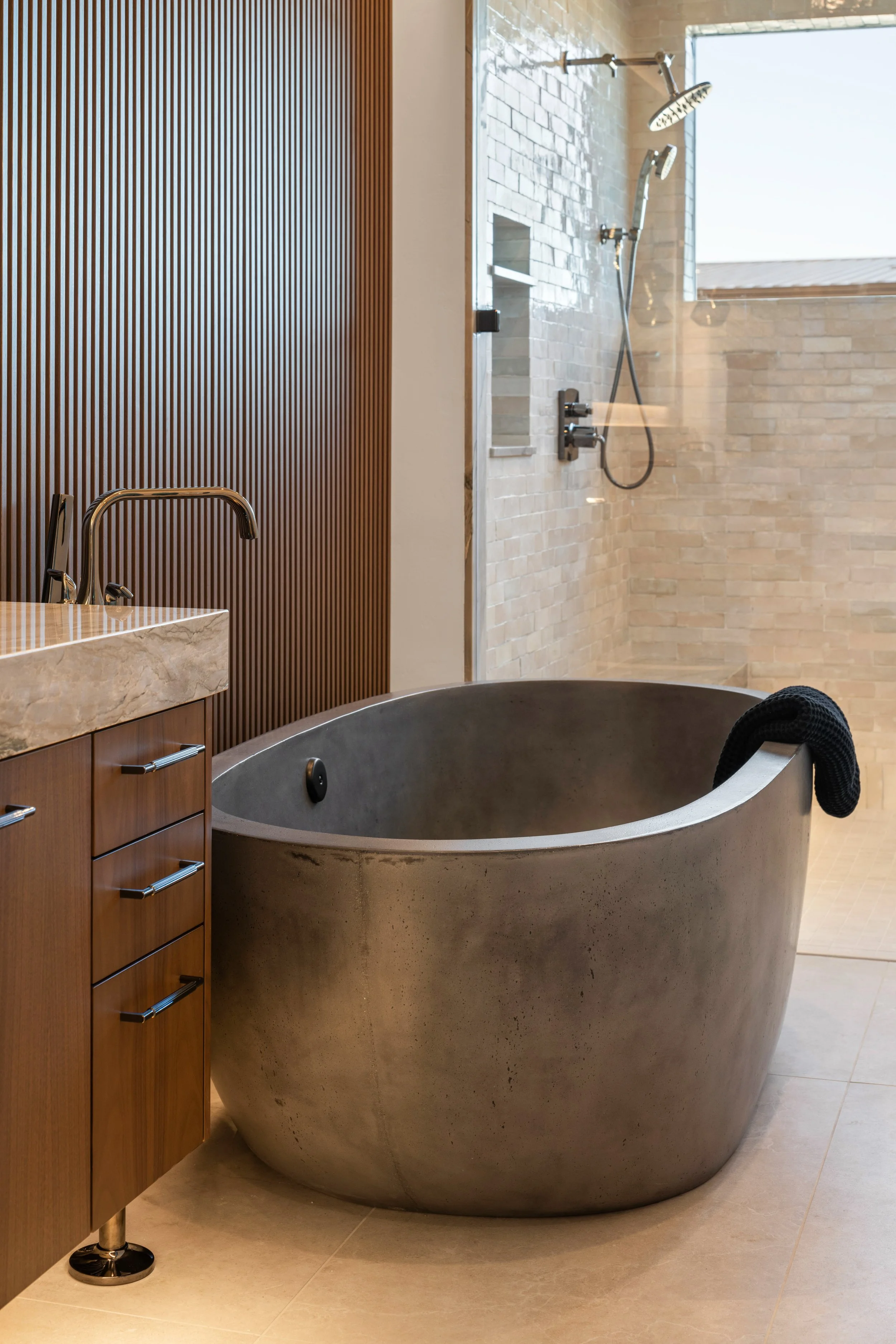 Close-up view of a modern bathroom with a concrete bathtub, a wooden cabinet with metal handles, and a shower with white brick walls and a rainfall showerhead.