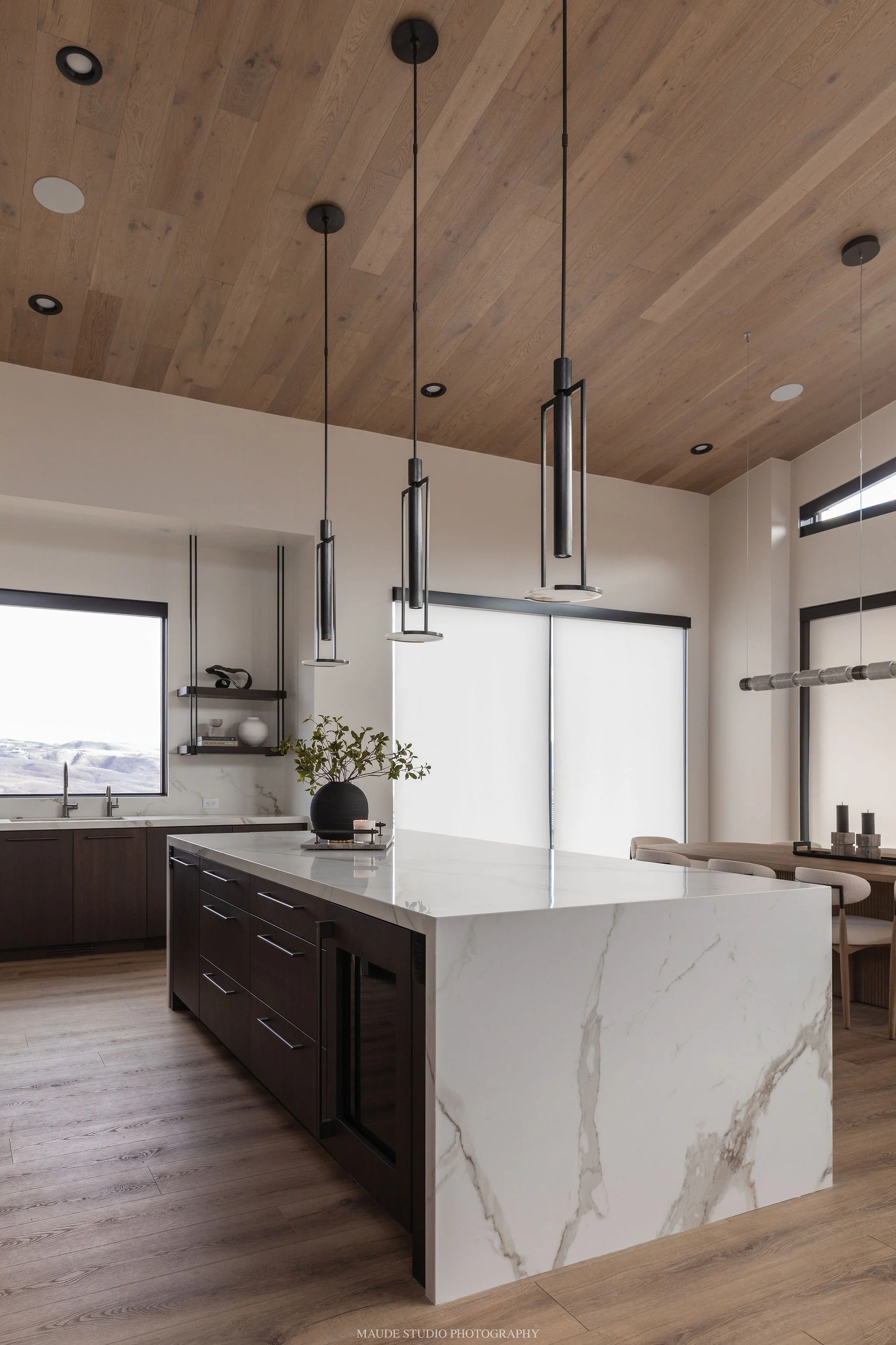 Modern kitchen with a large white marble island, dark wood cabinets, pendant lights, and a wooden ceiling.