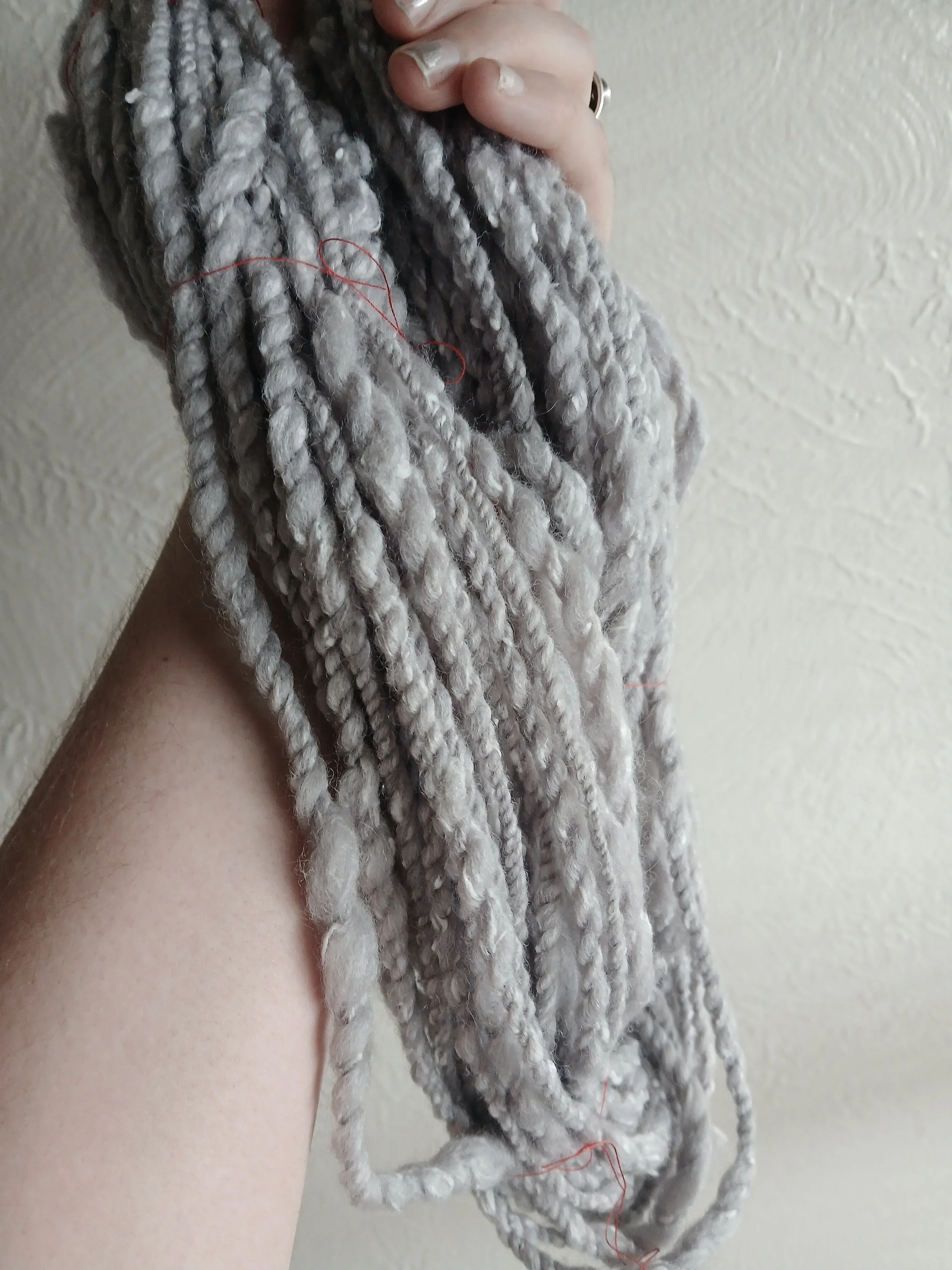 A hand holding up a hank of gray yarn