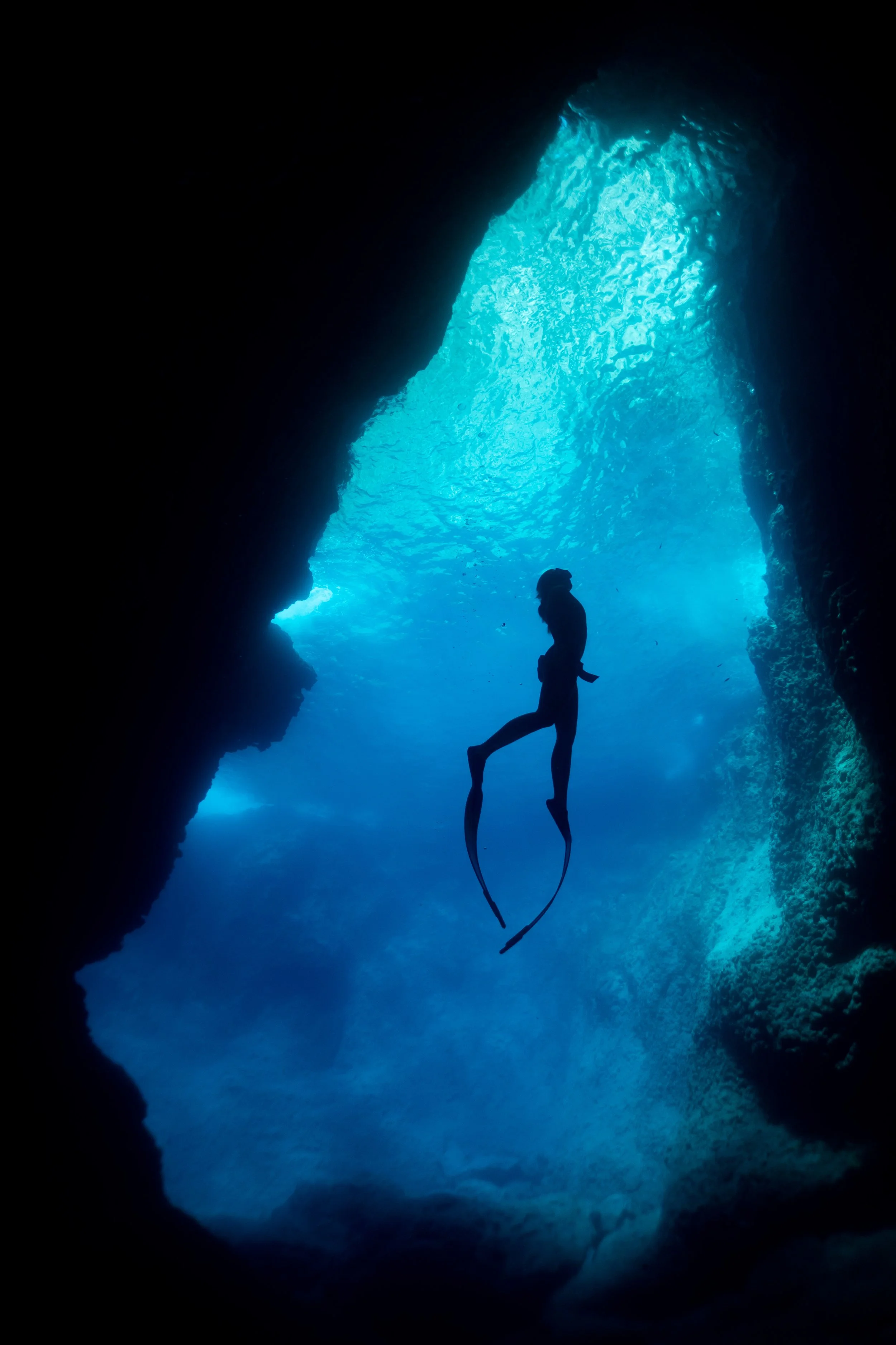 A person is free falling in a deep underwater cave with blue water and rocky walls, creating an adventurous scene.