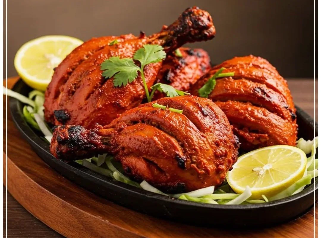 Tandoori chicken served on a black skillet with lemon slices and cilantro garnish.