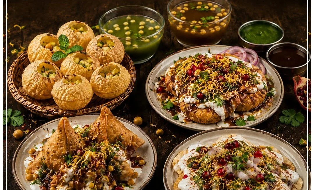 Assorted Indian dishes including stuffed pastries, chaat, and various chutneys and toppings on a dark wooden table.