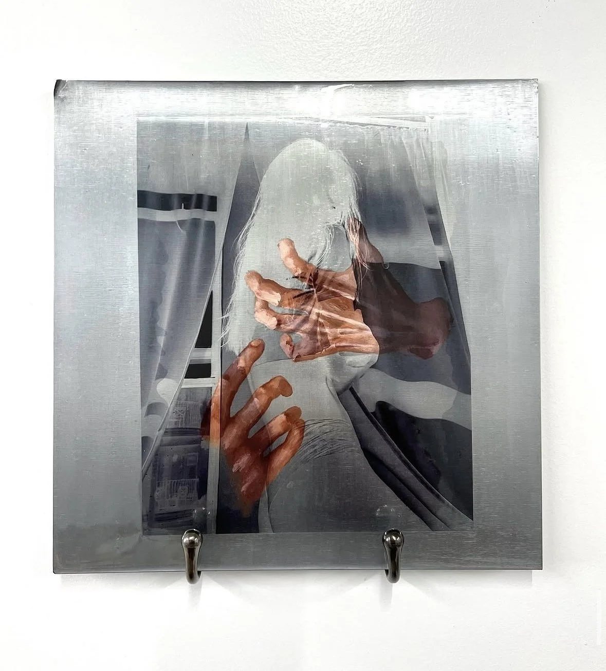 A metal box with a transparent front, showing a distorted reflection of a person with white hair taking a selfie with a smartphone.