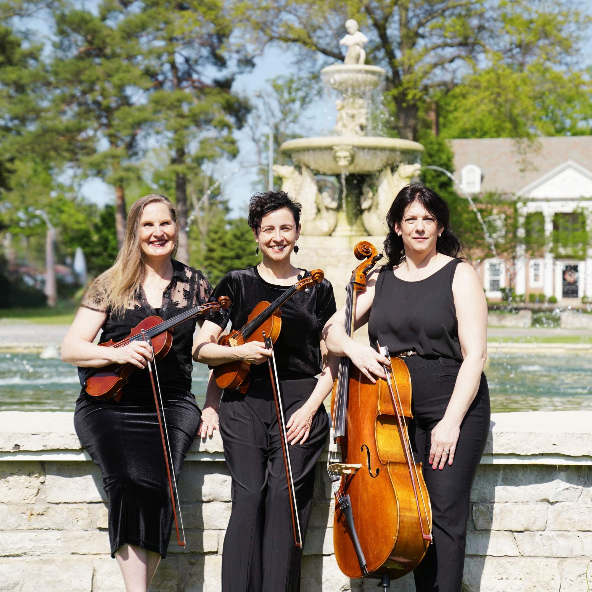 Three Maple Strings musicians with violins and cello near an outdoor fountain, representing live string music in the Kansas City area.