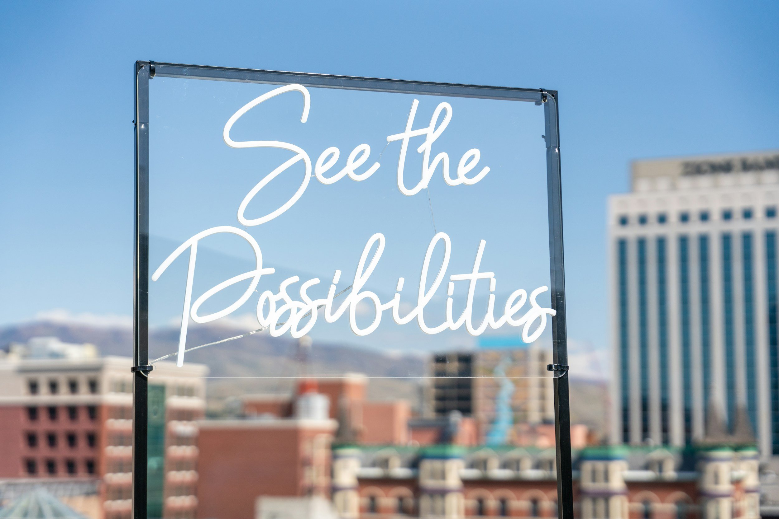 Neon sign reading 'See the Possibilities' with a cityscape background and blue sky.