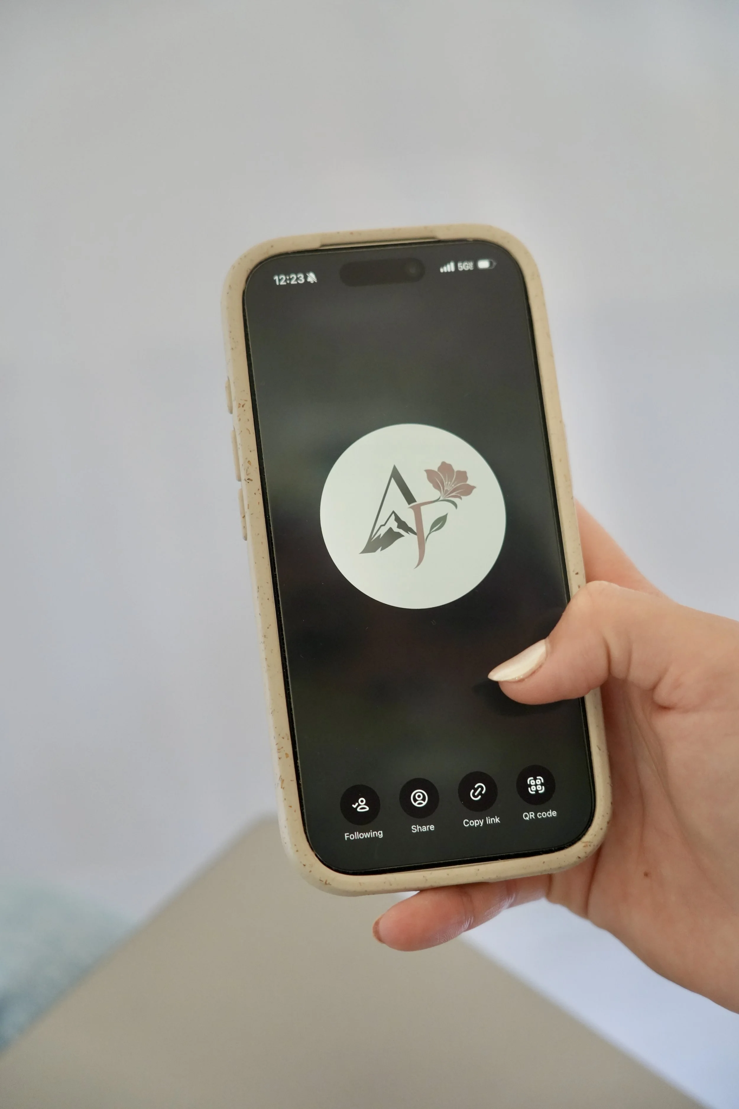A person holding a smartphone displaying a logo with a mountain, flower, and the letter 'A' on the screen.
