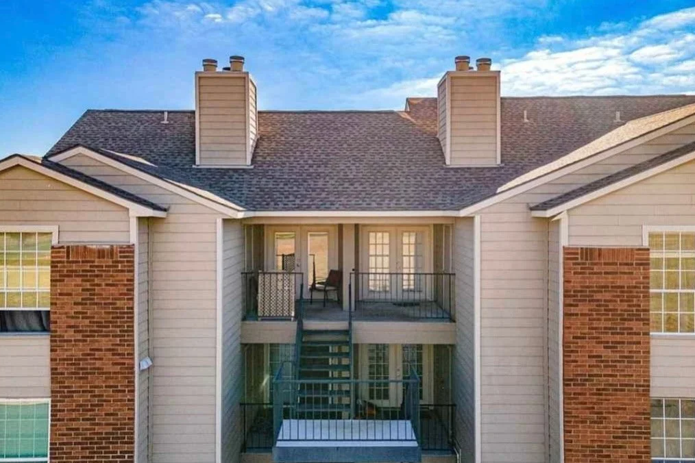 View of a residential apartment building with a balcony, brick chimneys, and multiple windows under a partly cloudy sky.