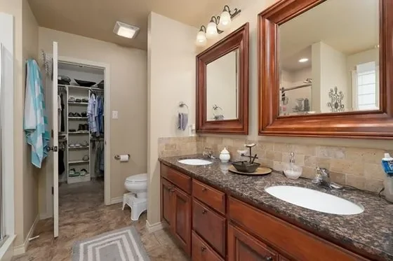 Bathroom with double sink vanity, large mirror, and walk-in closet in the background.