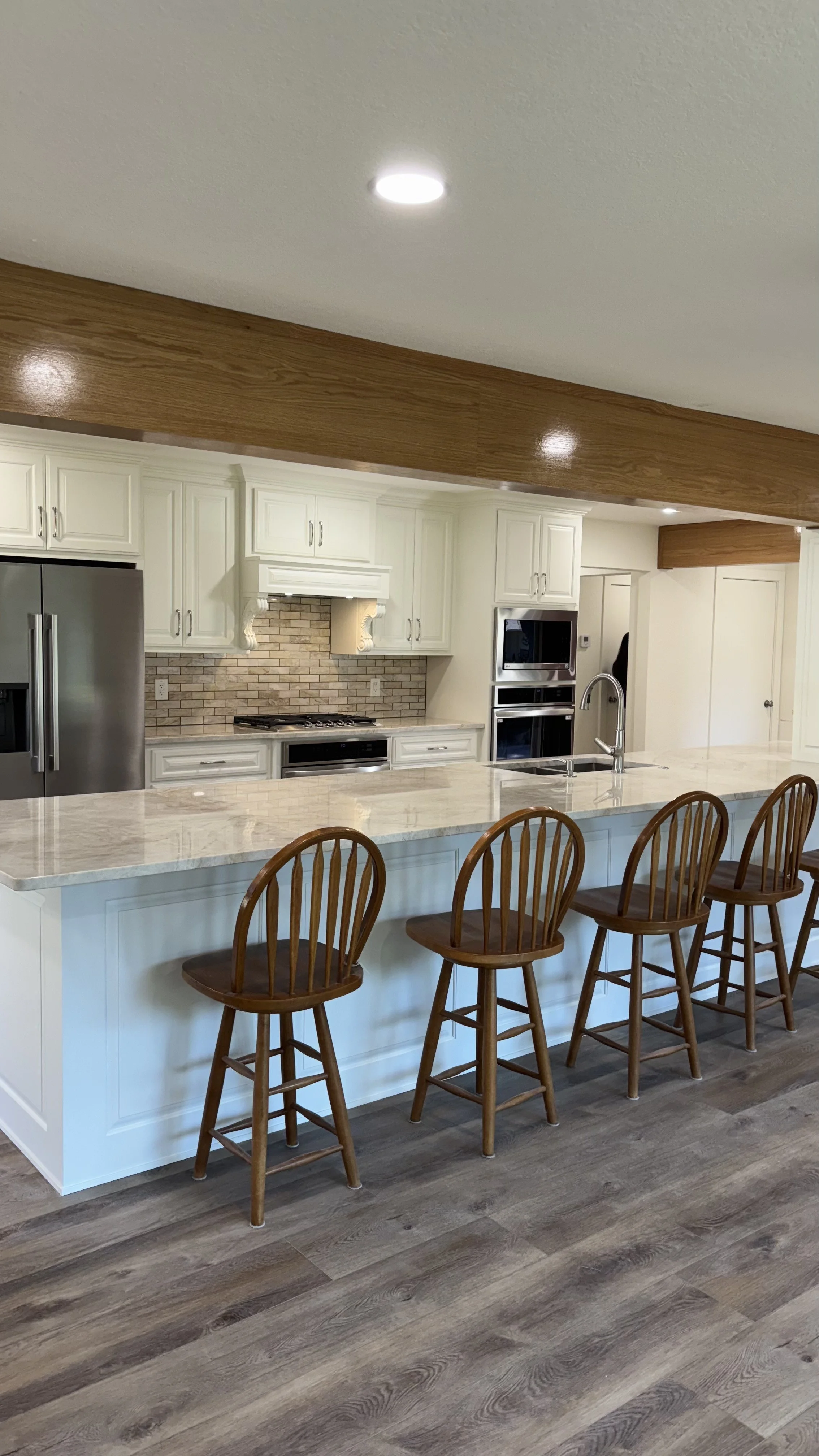 Kitchen with white cabinets, stainless steel refrigerator, brick backsplash, marble countertop island, and wooden bar stools.