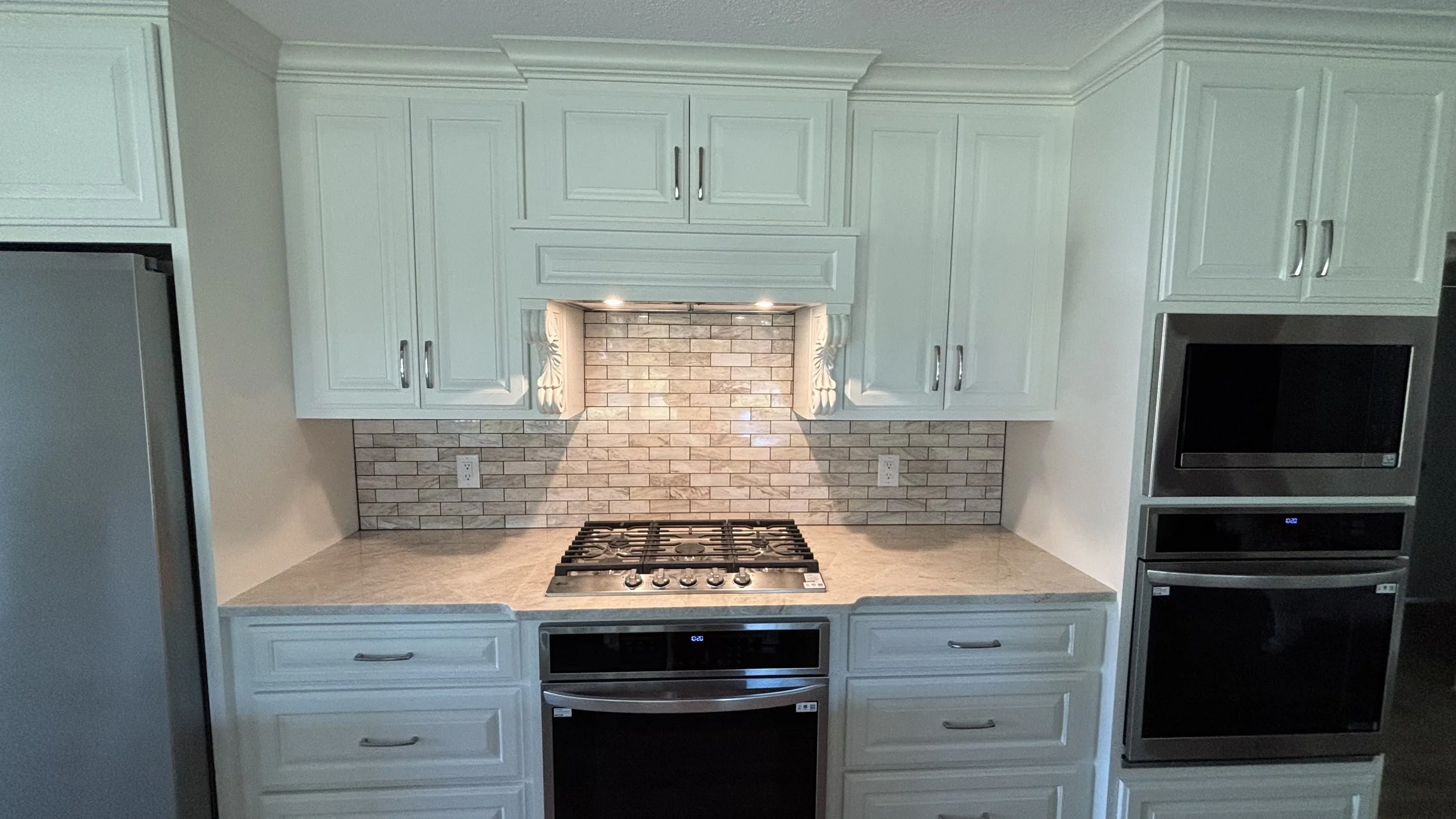 A modern kitchen with white cabinets, a gray countertop, a brick backsplash under the cabinets, a built-in gas stove, and an over-the-range microwave.