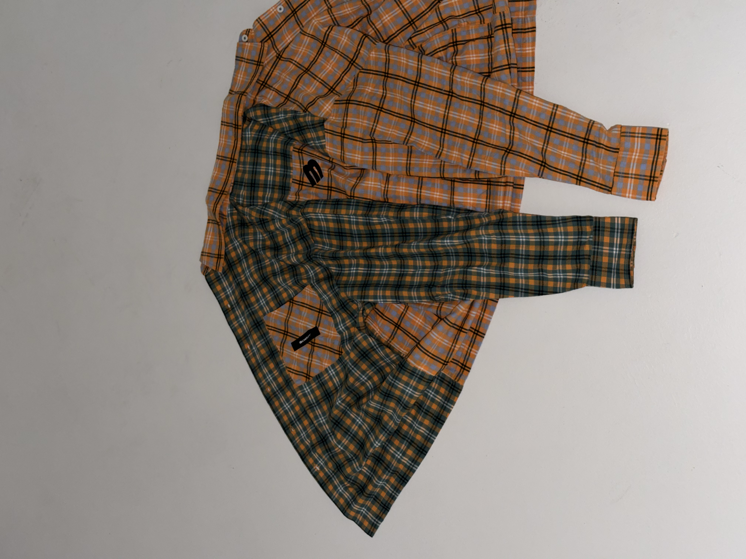 Three pairs of plaid shorts hanging on a white wall. The shorts have different colors and patterns, with one pair predominantly orange, one blue, and the other a mix of green and orange.