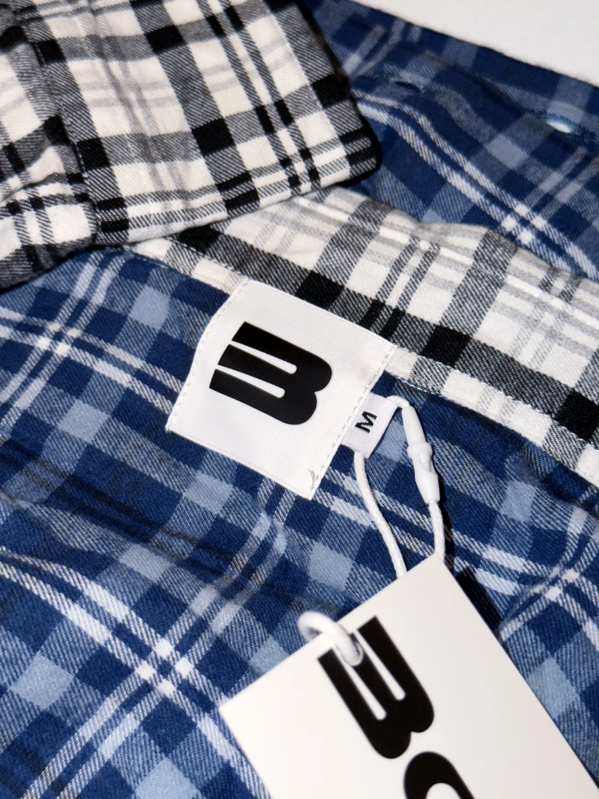 Close-up of blue and white plaid patterned shirt with a white label that has bold black text.