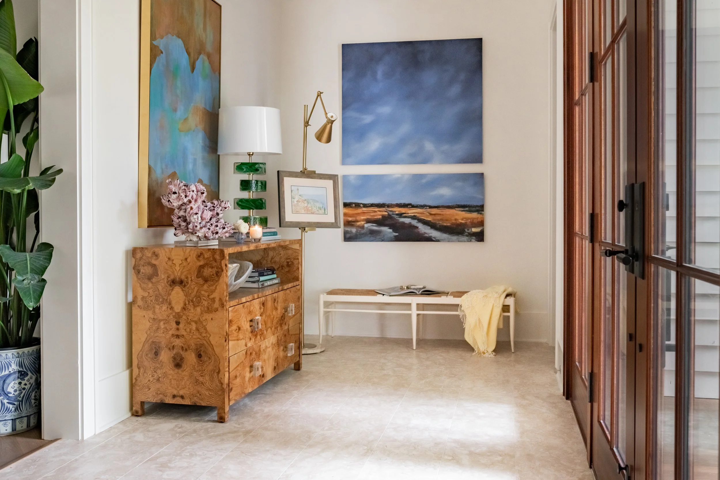 Entrance area with a wooden cabinet, framed pictures, and two large abstract landscape paintings on the wall.